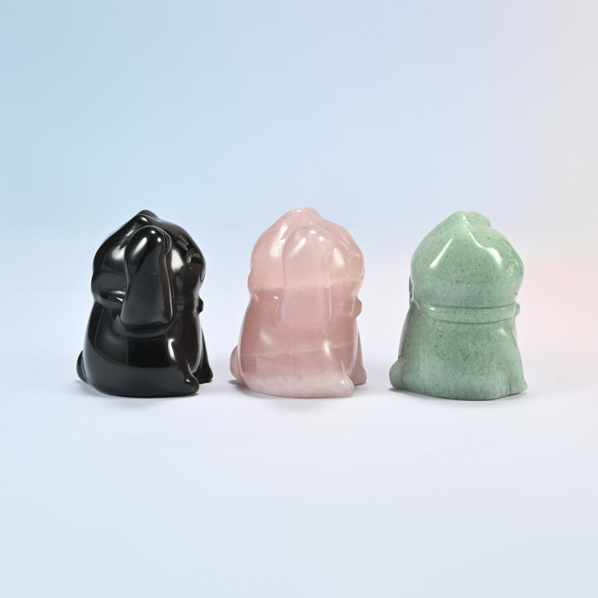 Back view of three waving cat crystal carvings in black, pink and green stone