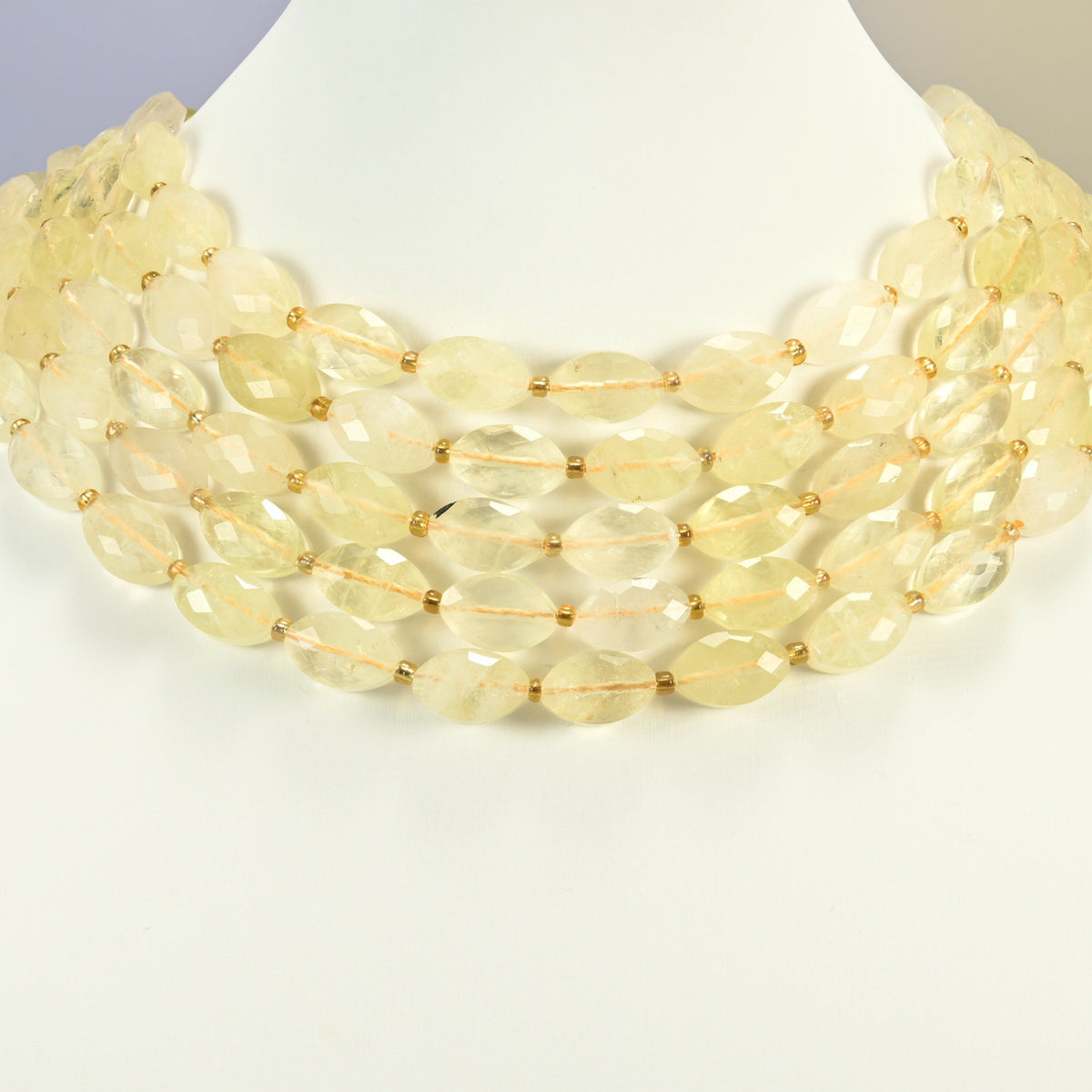 Citrine faceted flat oval strands arranged as a layered collar on a white display bust, light yellow beads across the neck