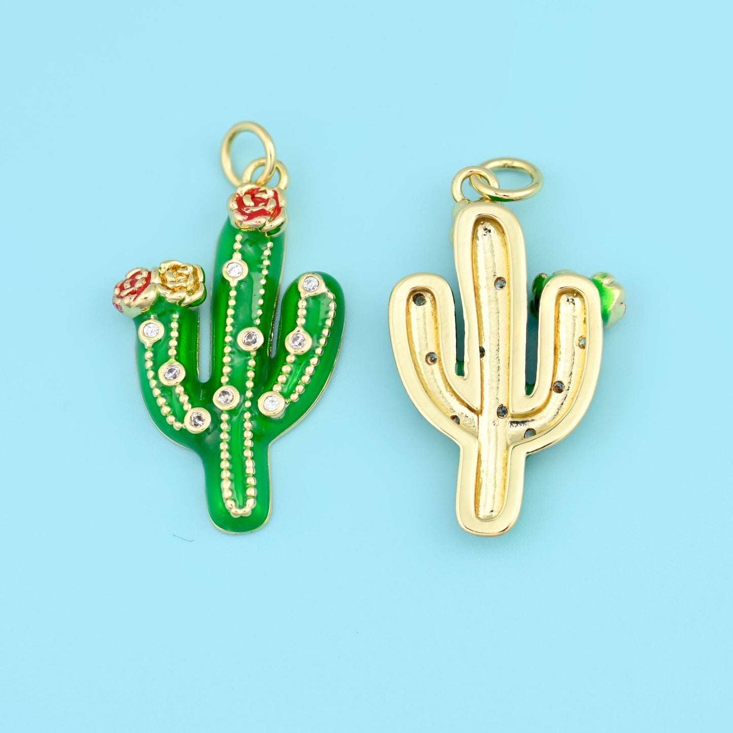 A three-armed saguaro in glossy enamel with a tiny coral red bloom at the crown, ribbed down the body with dotted lines of…