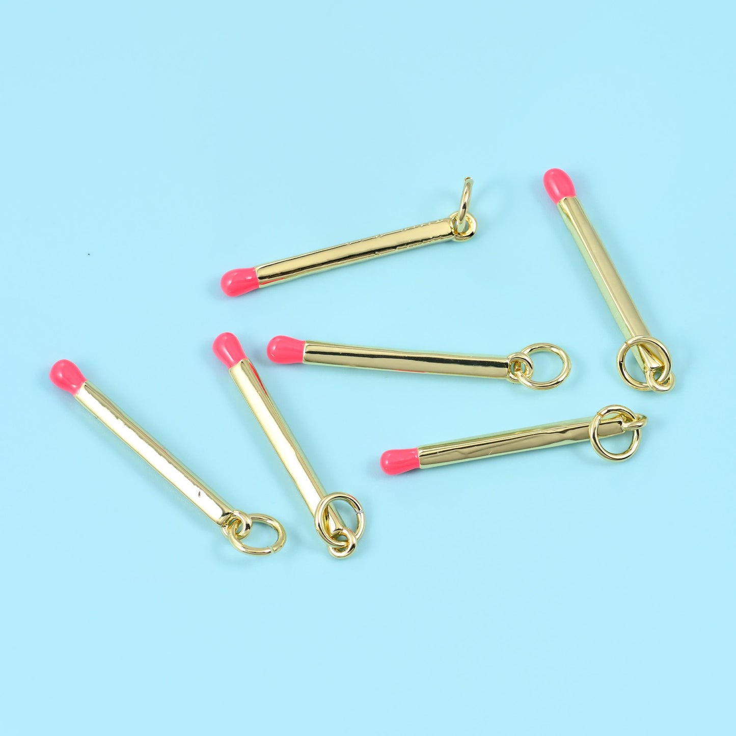 Enamel matchstick pendant in coral pink, six gold bars with coral tips angled across a blue background.