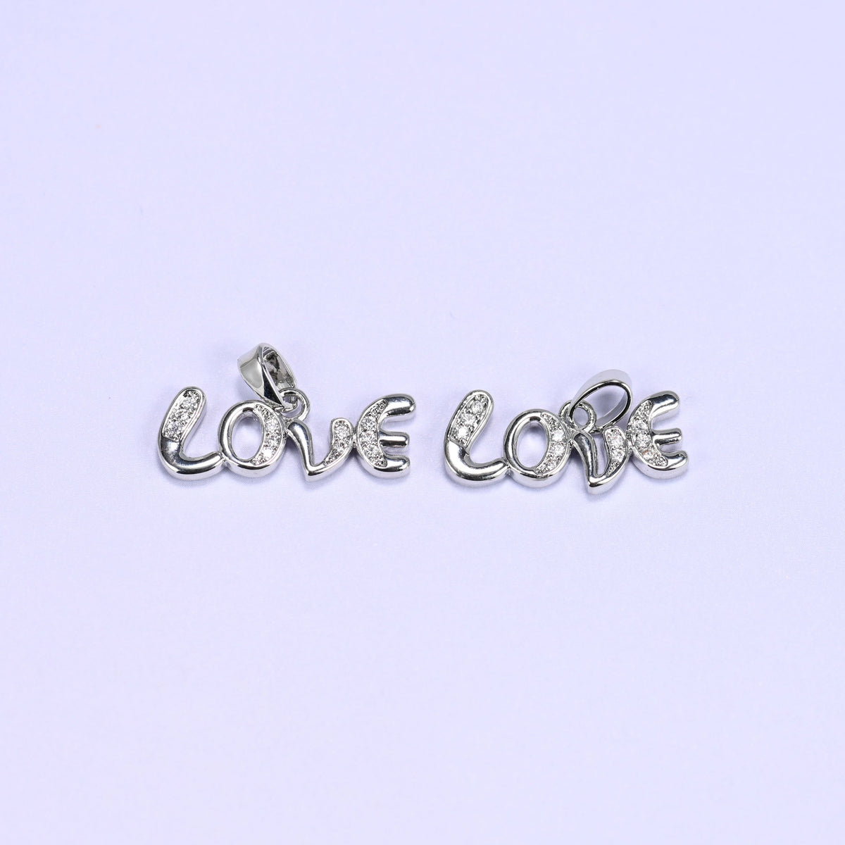 Two silver-tone Love letter zirconia charms lying side by side, the cursive Love script lined with small clear pave stones.