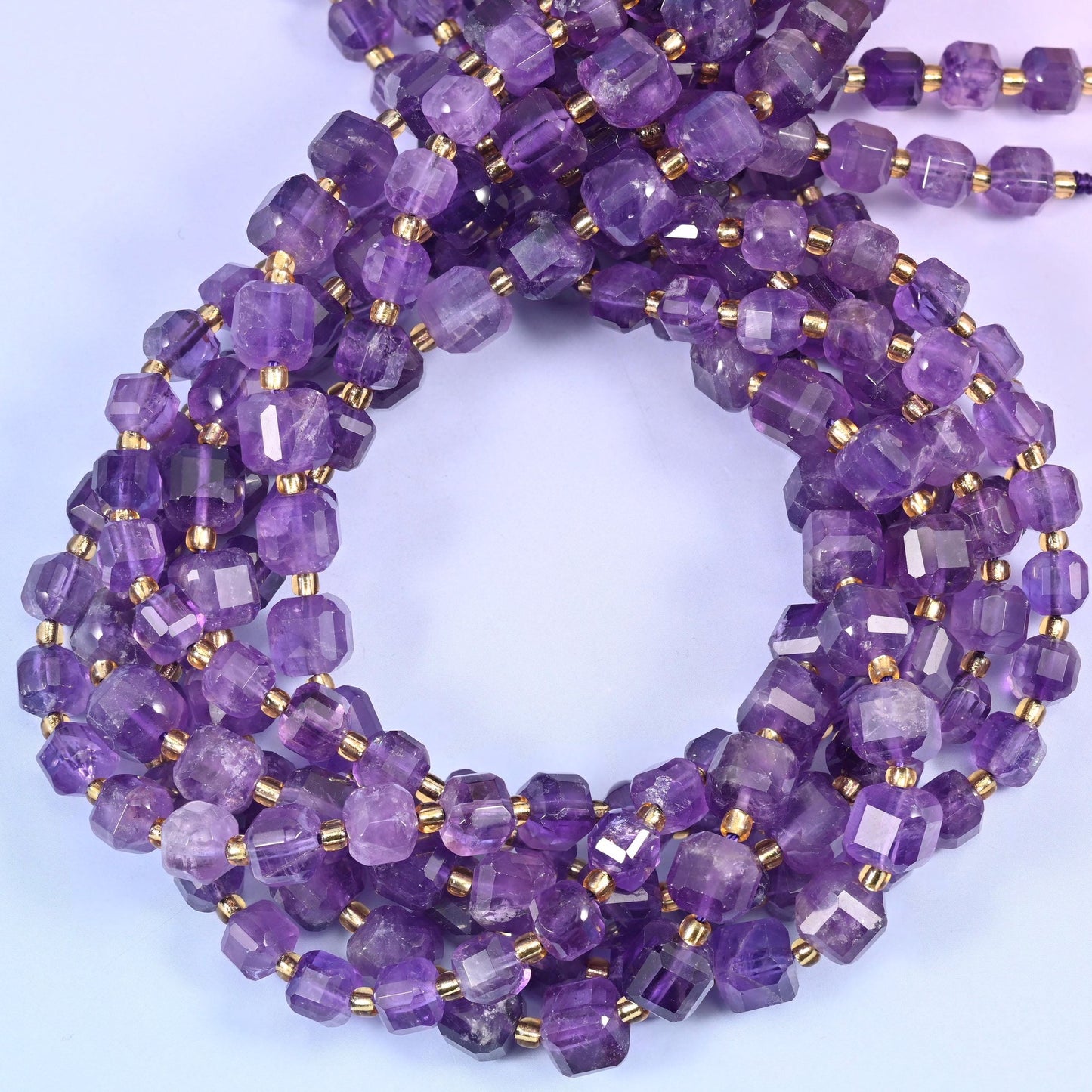 Clear mid-purple stone with pale near-white zoning running through it, squared off into cubes with every corner cut back so light bounces off several planes at once.