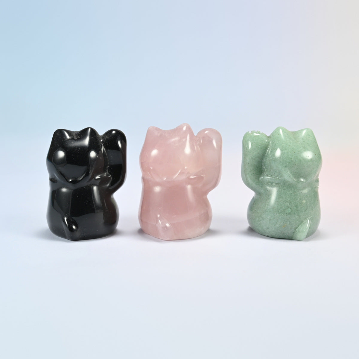 Three maneki neko crystal cats in black obsidian, rose quartz and green aventurine turned at an angle