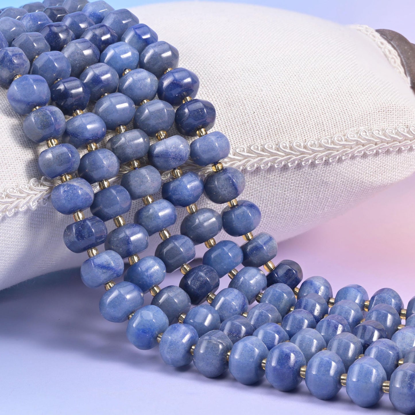 Soft denim-blue Blue Aventurine pumpkin rondelles heaped against a cream cushion, each bead ringed by a thin brass spacer