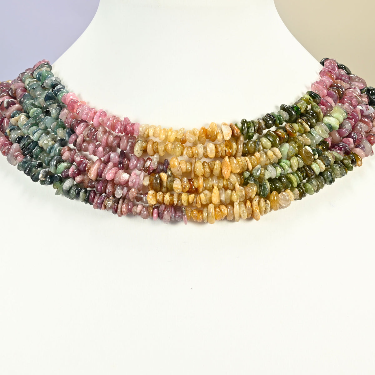 Multicolor tourmaline chip strands arranged as a layered collar on a white display bust, green, pink and golden yellow blocks across the neck