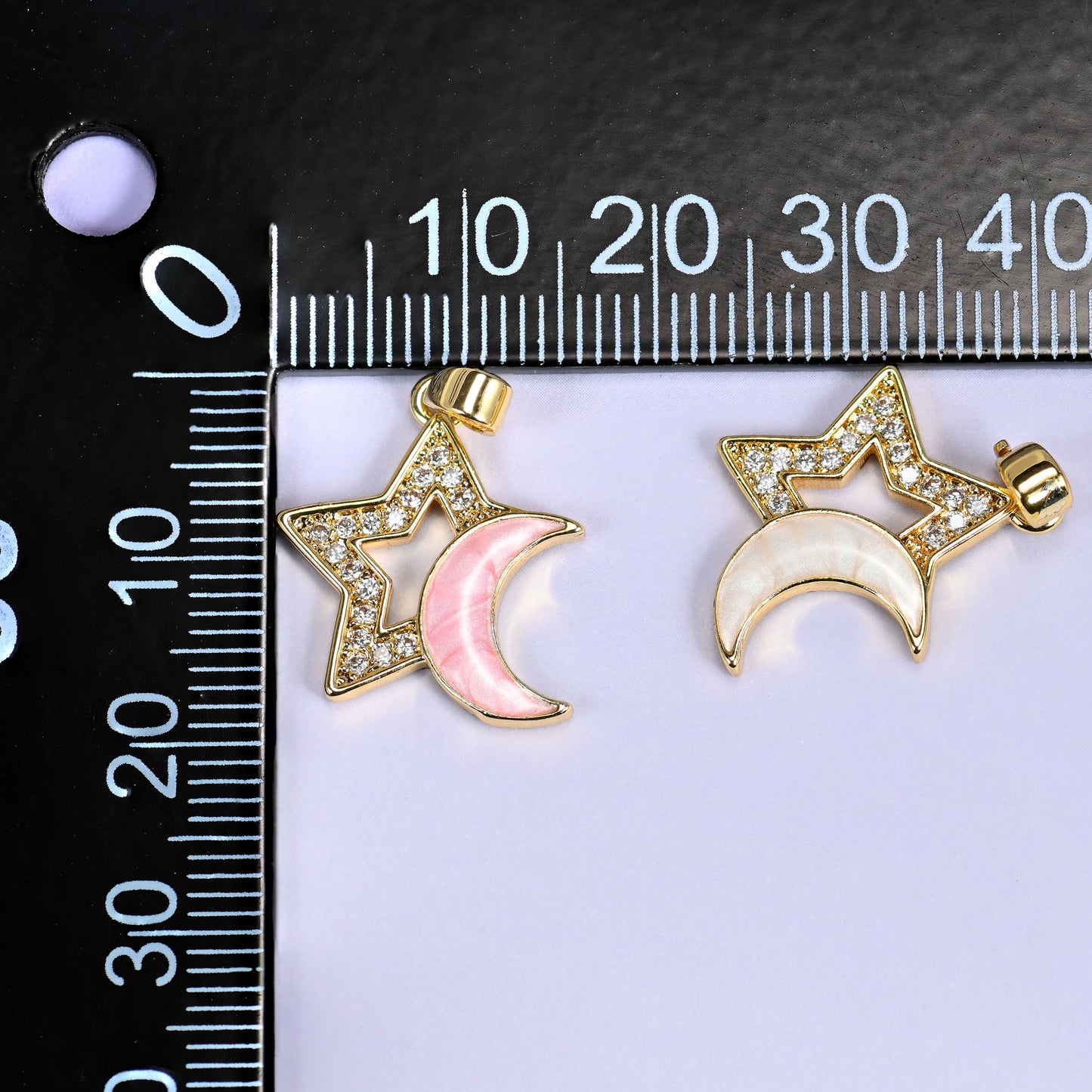 Pink and white Star Shell Moon Zirconia Charms on a black millimeter ruler, both colorways shown together against the mm markings.