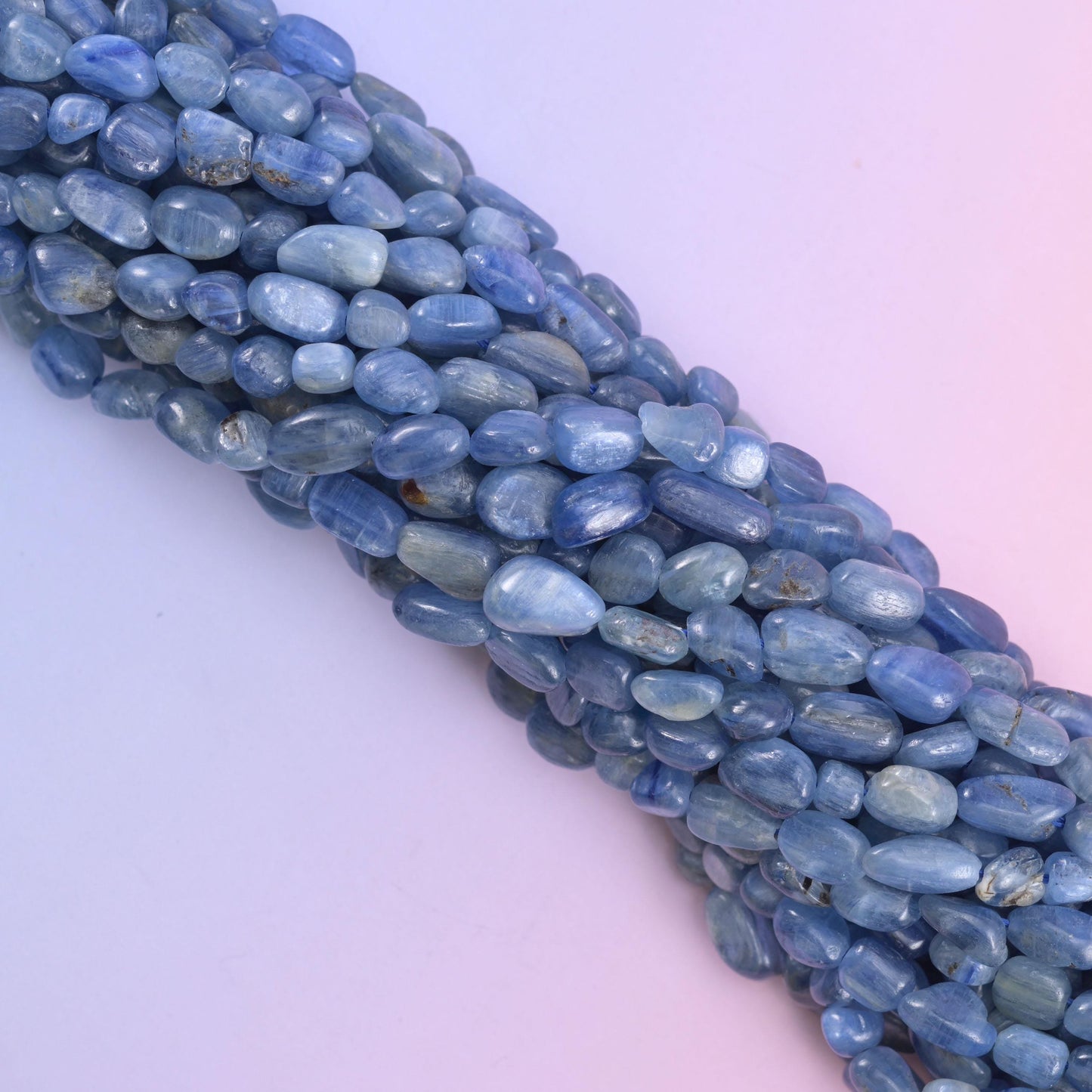Diagonal sweep of kyanite nugget strands across a pink-lilac gradient background