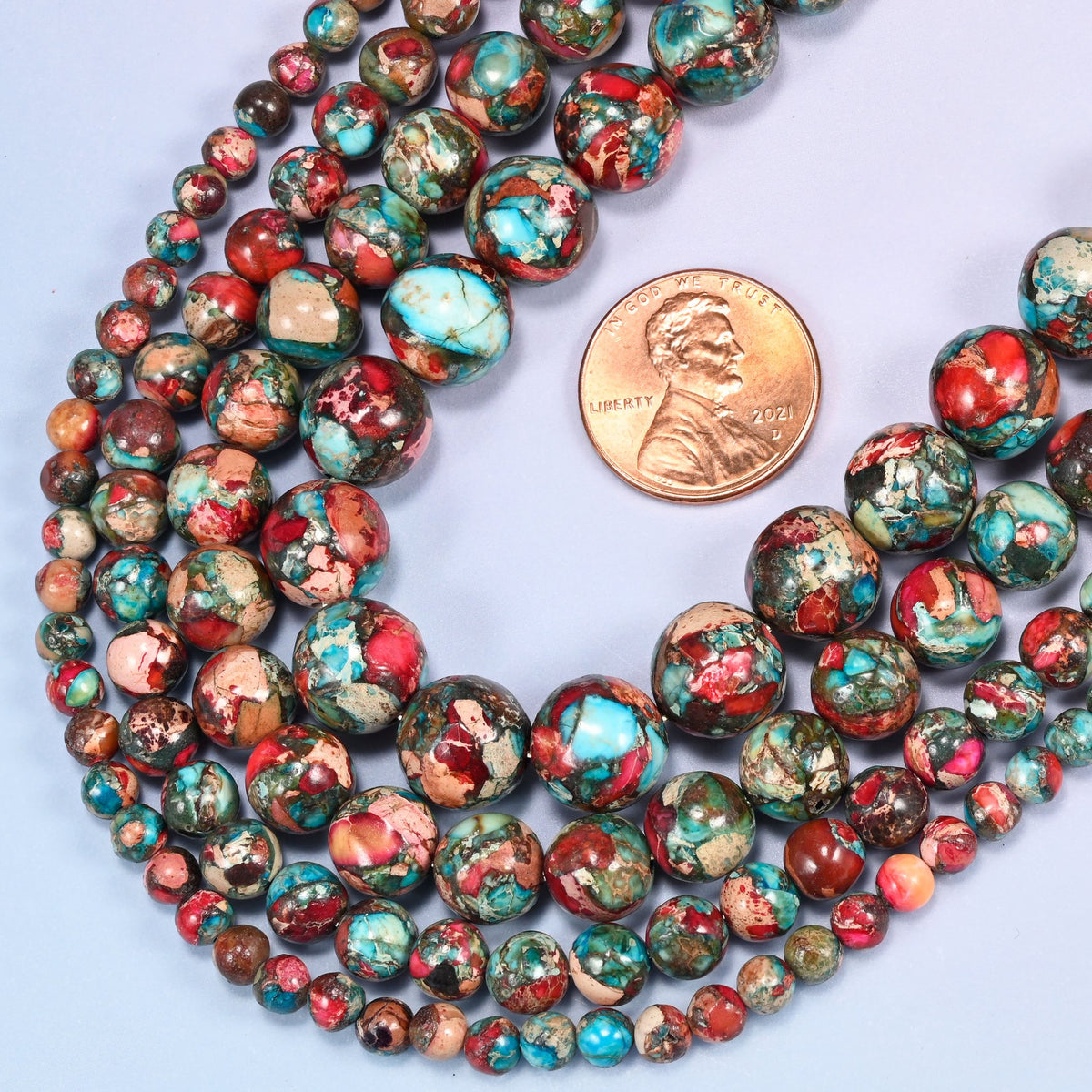 Red sea sediment jasper smooth round beads coiled loosely, shown with a US penny resting on the strands for scale.