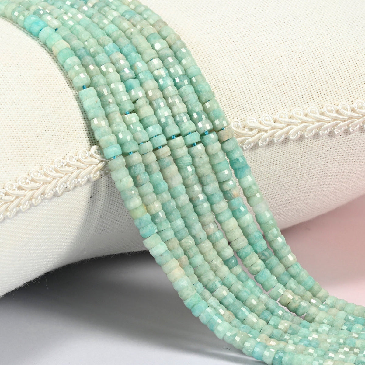 Green amazonite faceted heishi disc beads 2x4mm, several strands draped over a white cushion