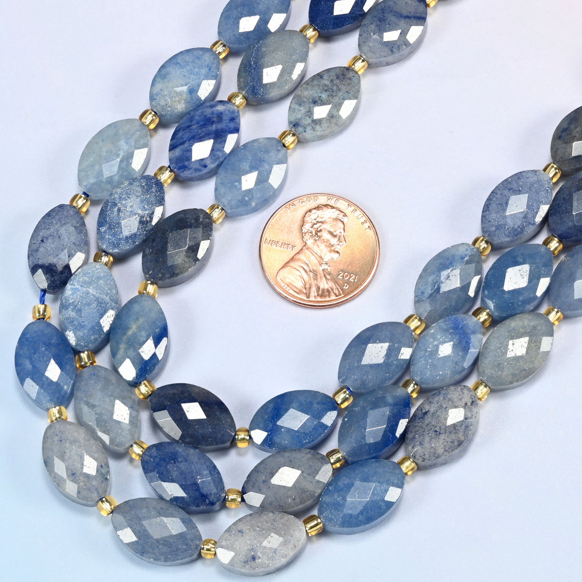 Close view of blue aventurine faceted flat oval strands curving beside a US penny for scale