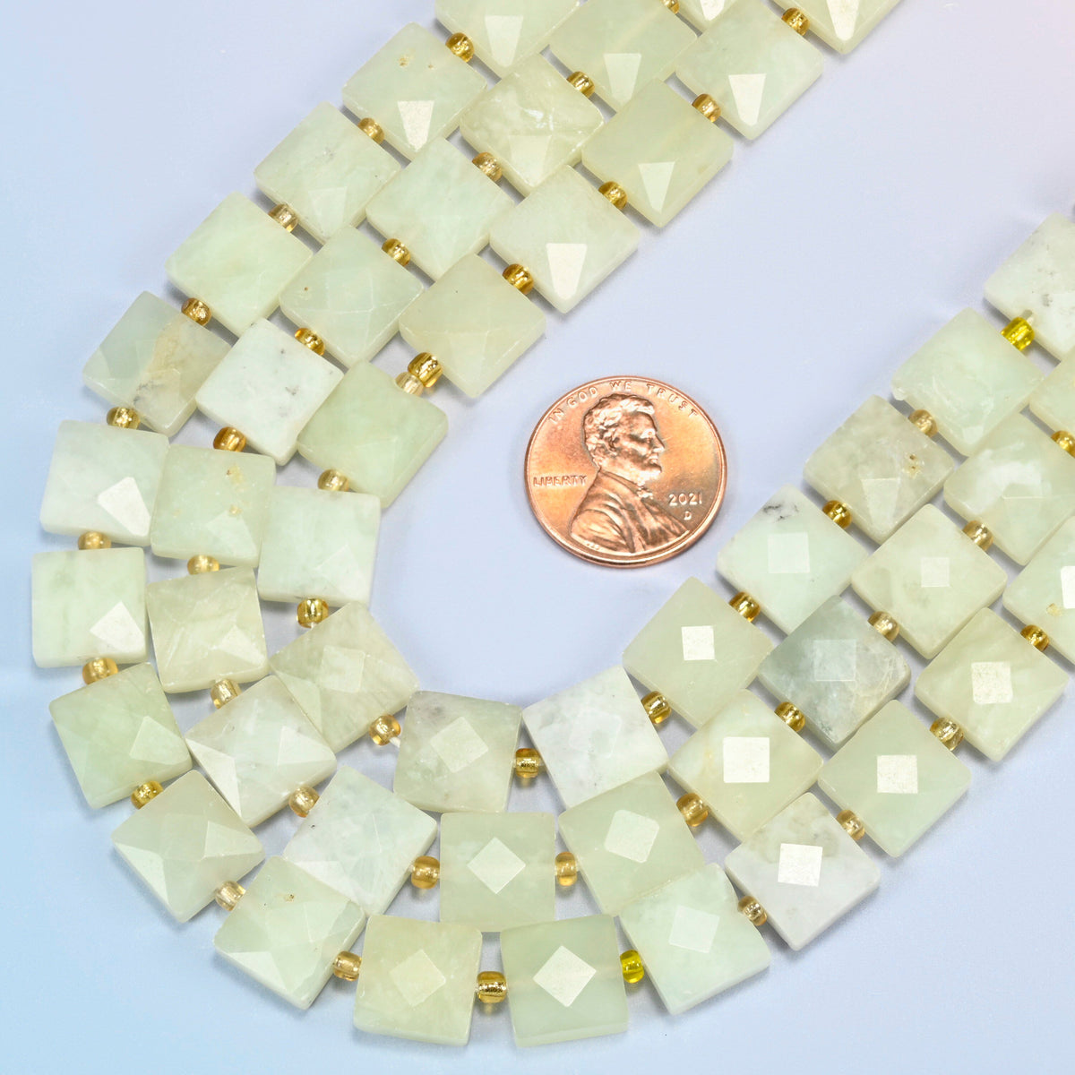 Close view of New Jade faceted flat square strands curving beside a US penny for scale