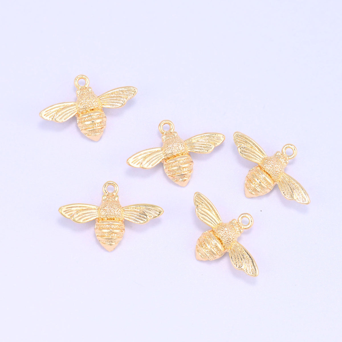 Small gold charms bee, five 18K gold plated bee charms grouped together on a lilac backdrop