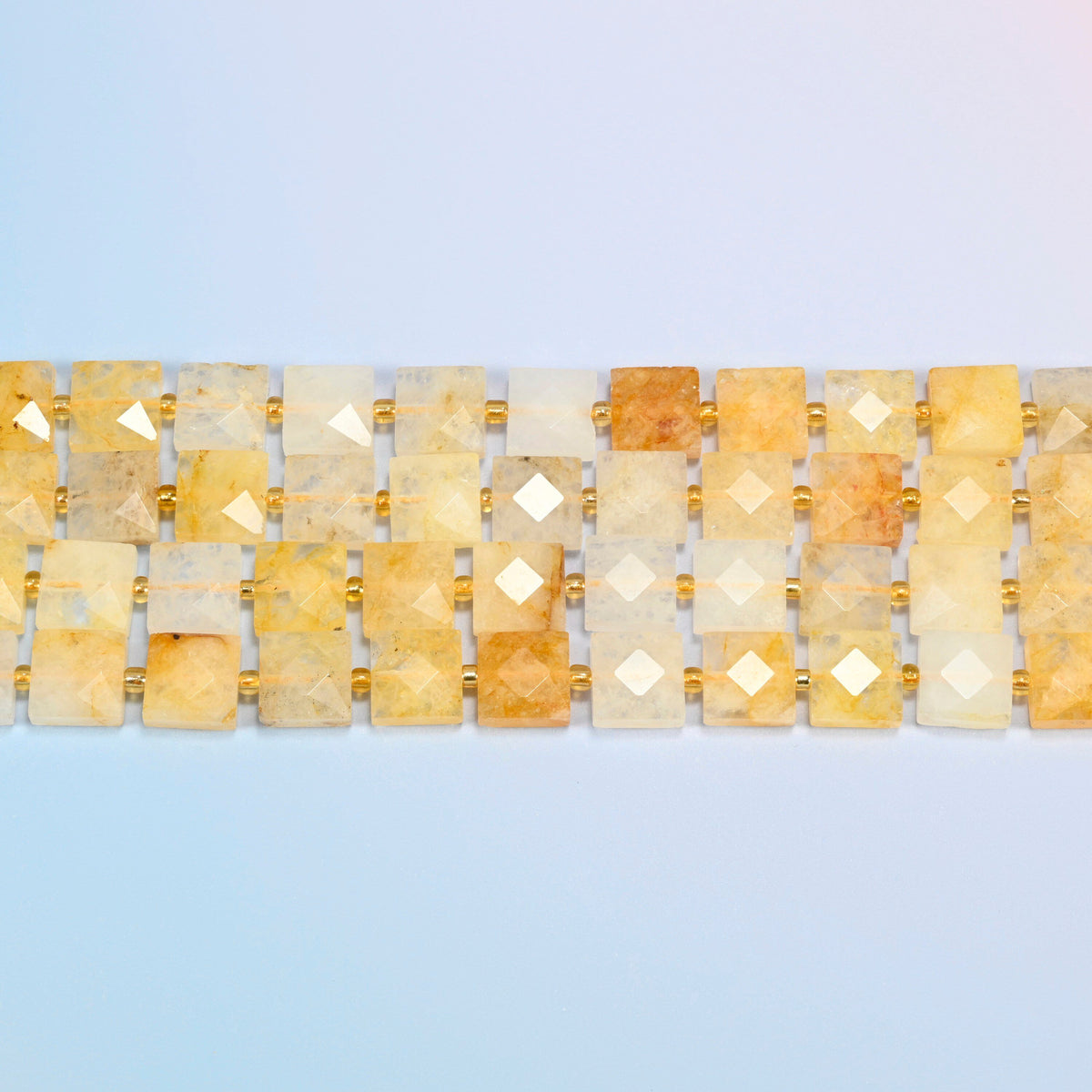 Several strands of natural golden healer quartz faceted flat square beads laid in straight rows