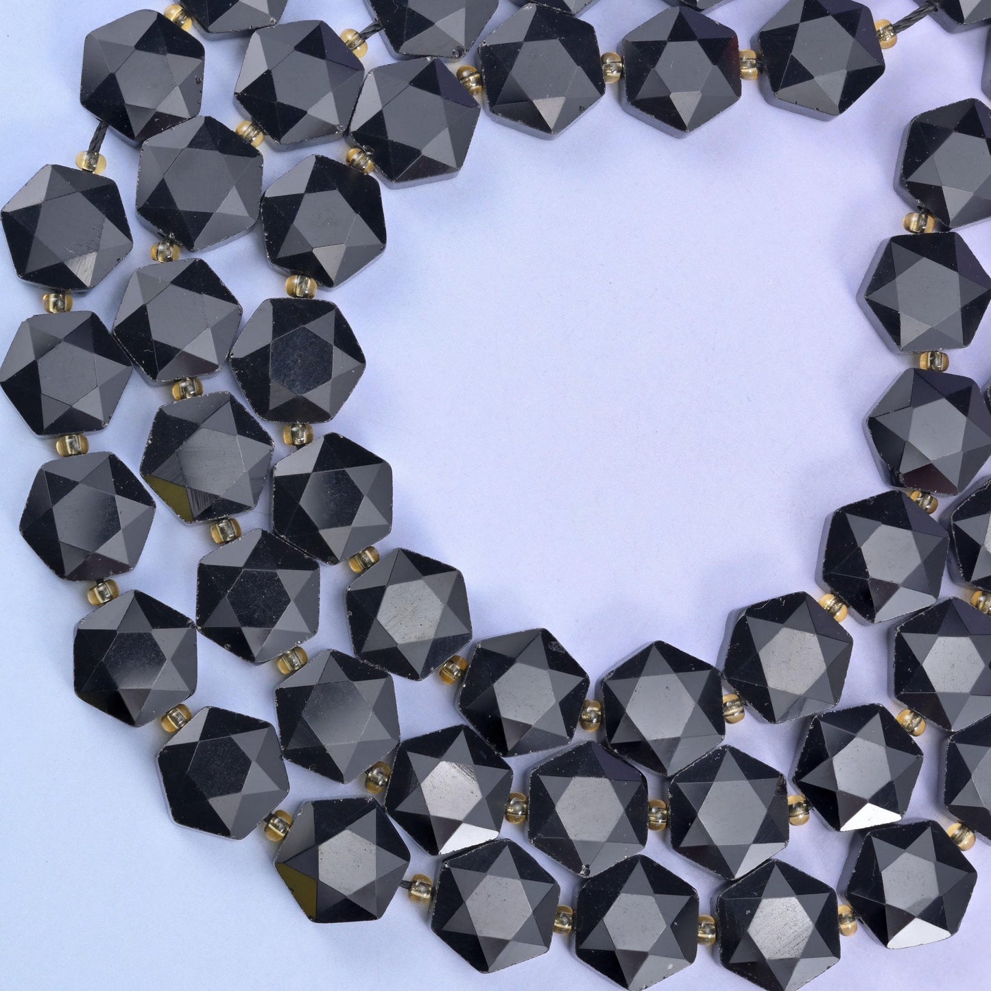 Open circle of black obsidian hexagons on pale lilac, facets bright against the flat faces