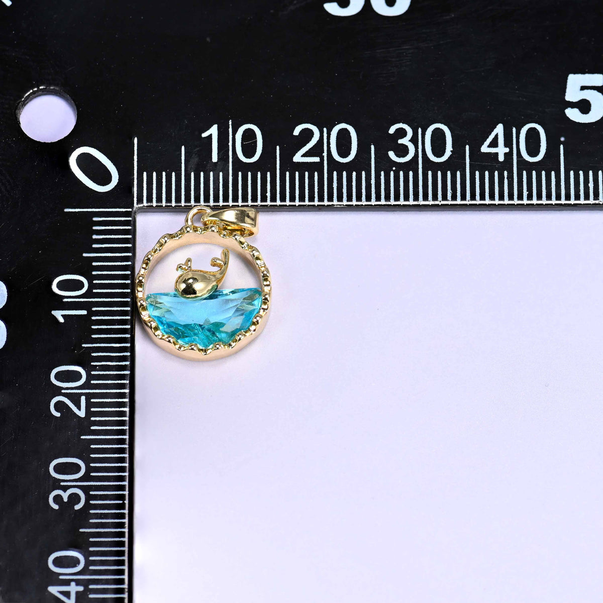 18K gold plated brass whale charm pendant with a gold whale silhouette diving into a faceted blue zirconia wave, set in a textured round frame.