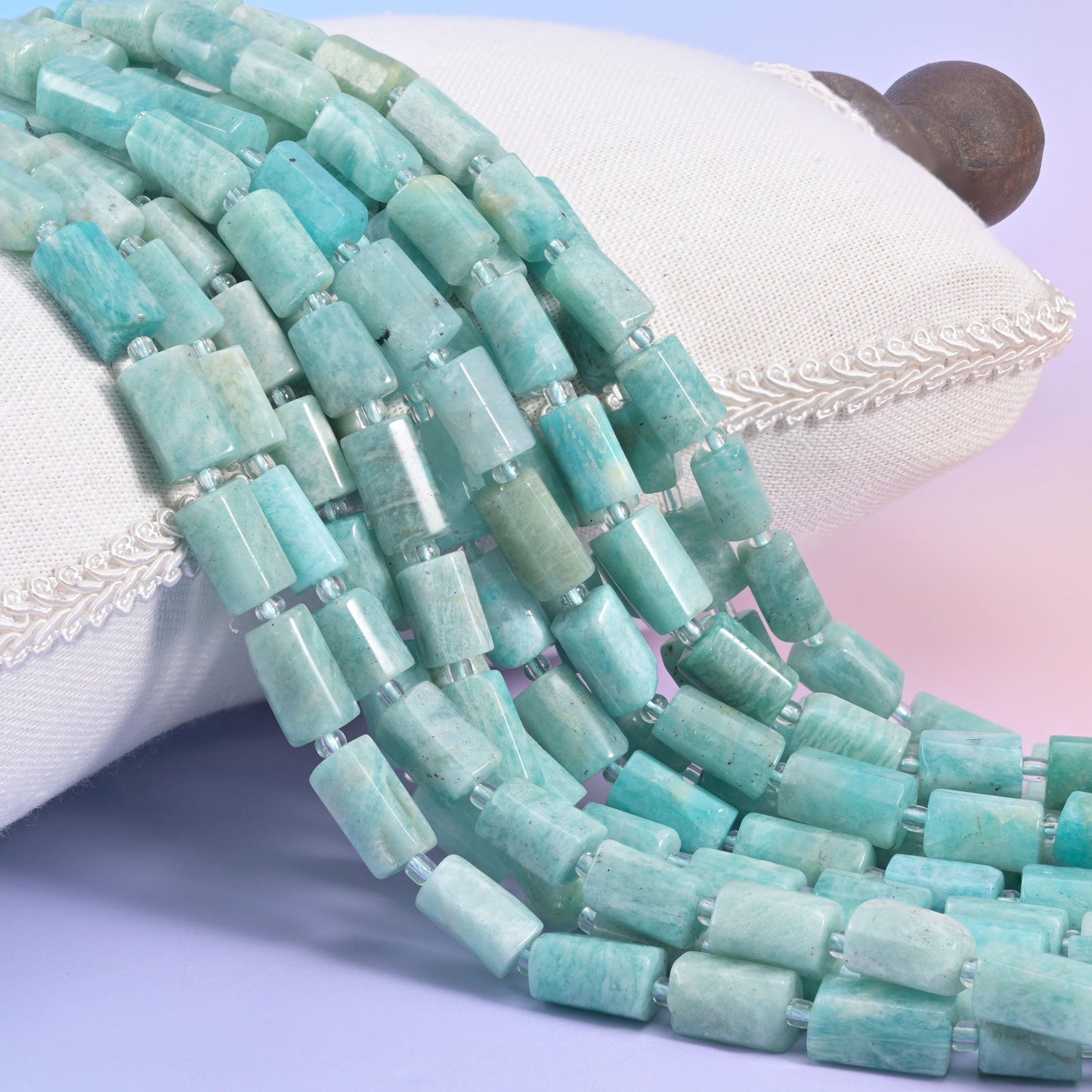 Several strands of pale aqua Blue Amazonite faceted tube beads draped over a white display pillow