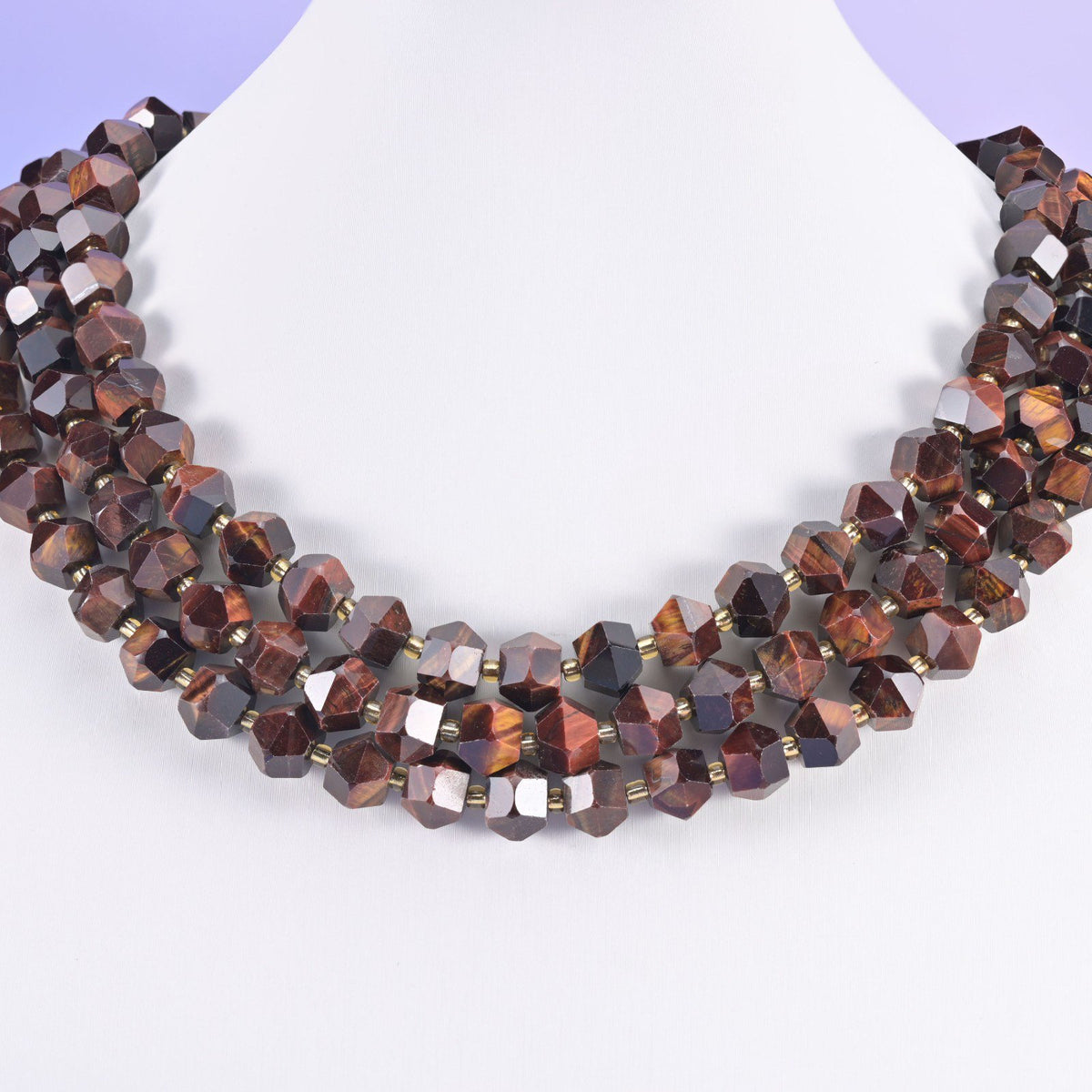 Faceted 8 sides diamond rhombus beads in dyed red tiger eye on a white neck display, three strands layered.