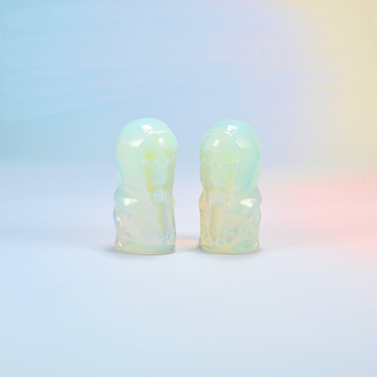 Two opalite hooded skull carvings with a milky glow and a soft blue sheen, man-made glass