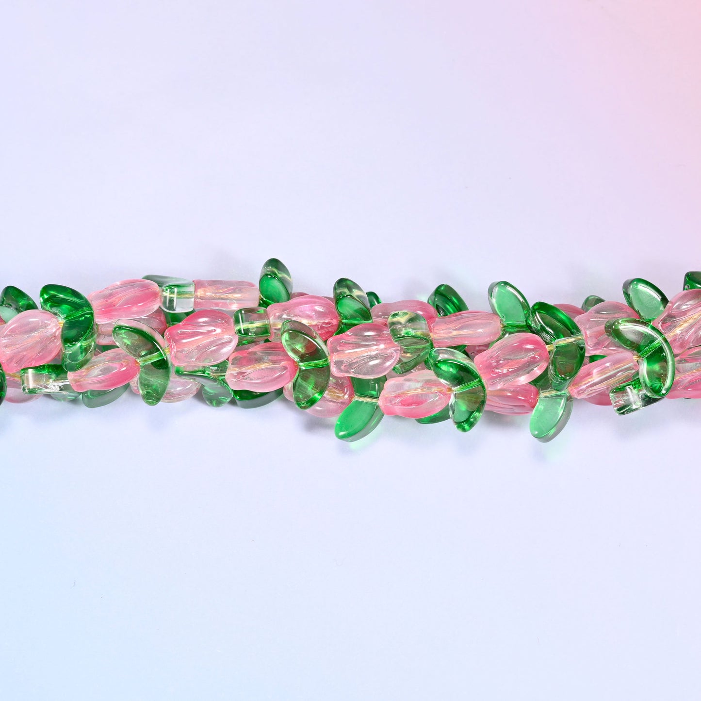 Wide view of a circular coil of pink tulip and green leaf glass bead strands on a lavender and pink gradient background.