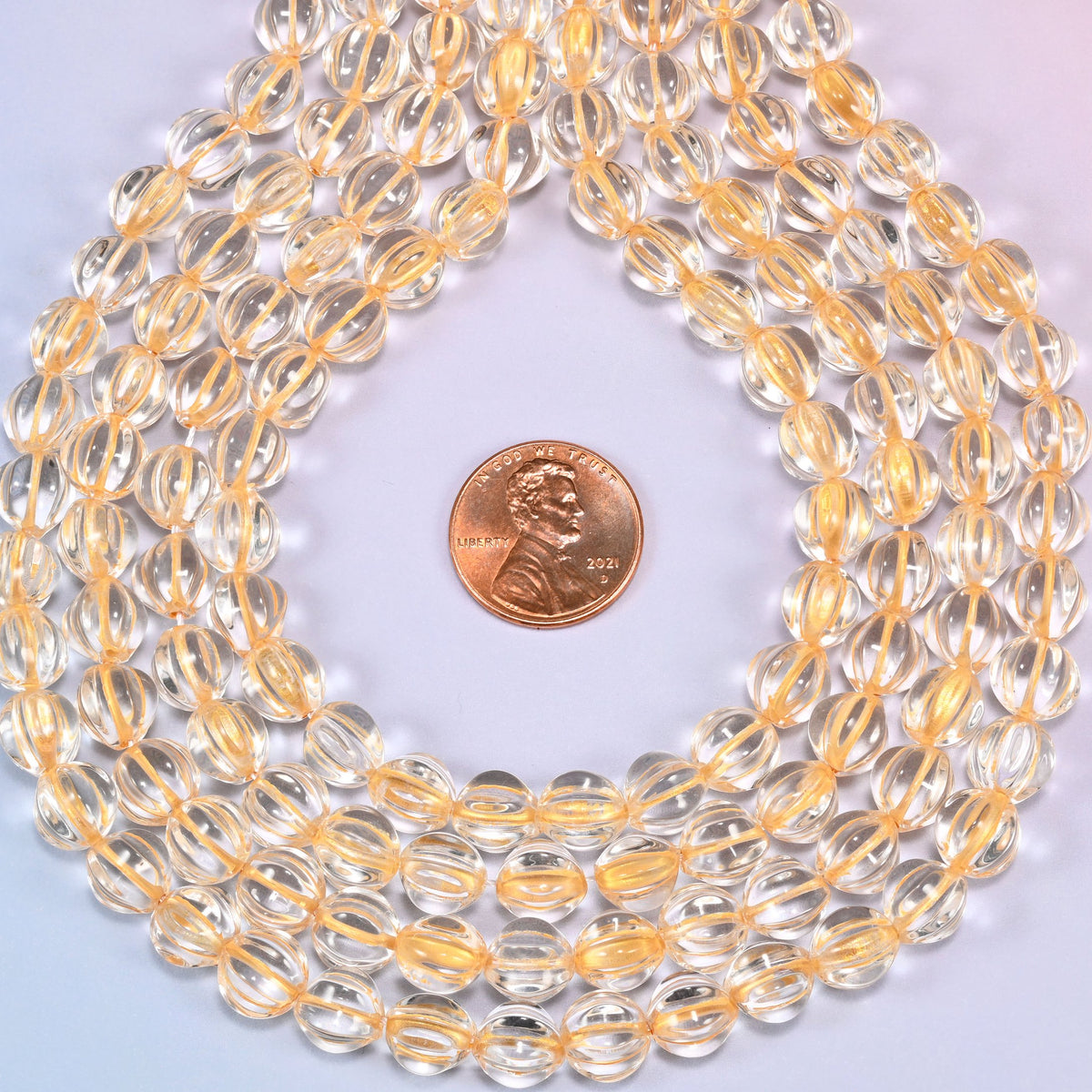 Clear gold pumpkin glass beads, 8mm melon rounds, strands laid in a gentle wave straight across the frame.