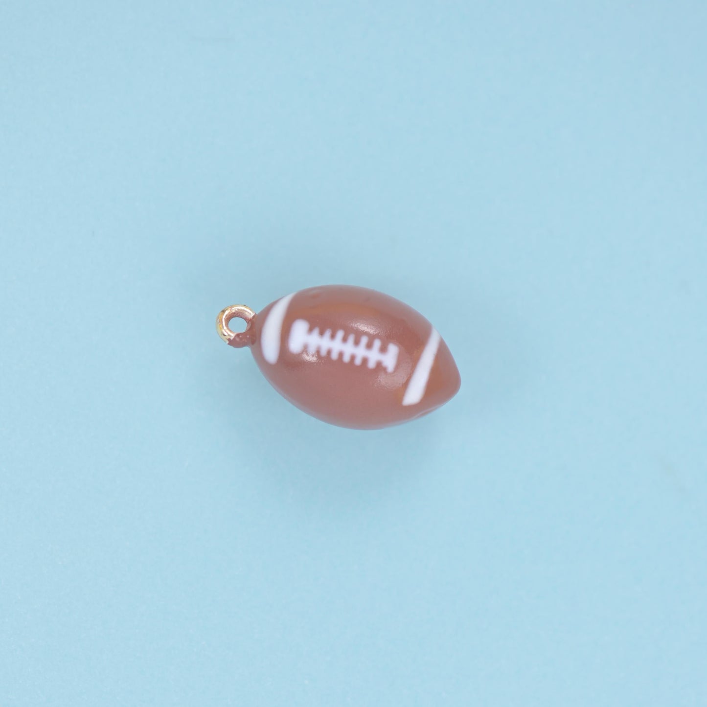 A fully rounded miniature football in glossy warm brown enamel with crisp white lacing and side stripes