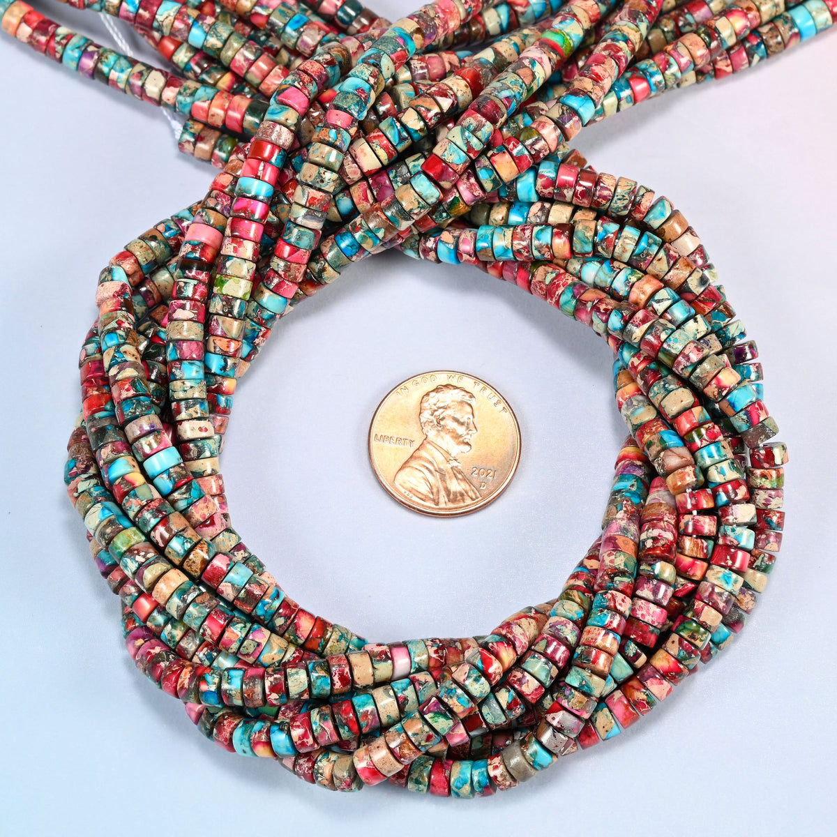 Dyed pink blue sea sediment jasper heishi disc beads 2x4mm coiled in a loop around a US penny for scale, close-up of the thin disc shape