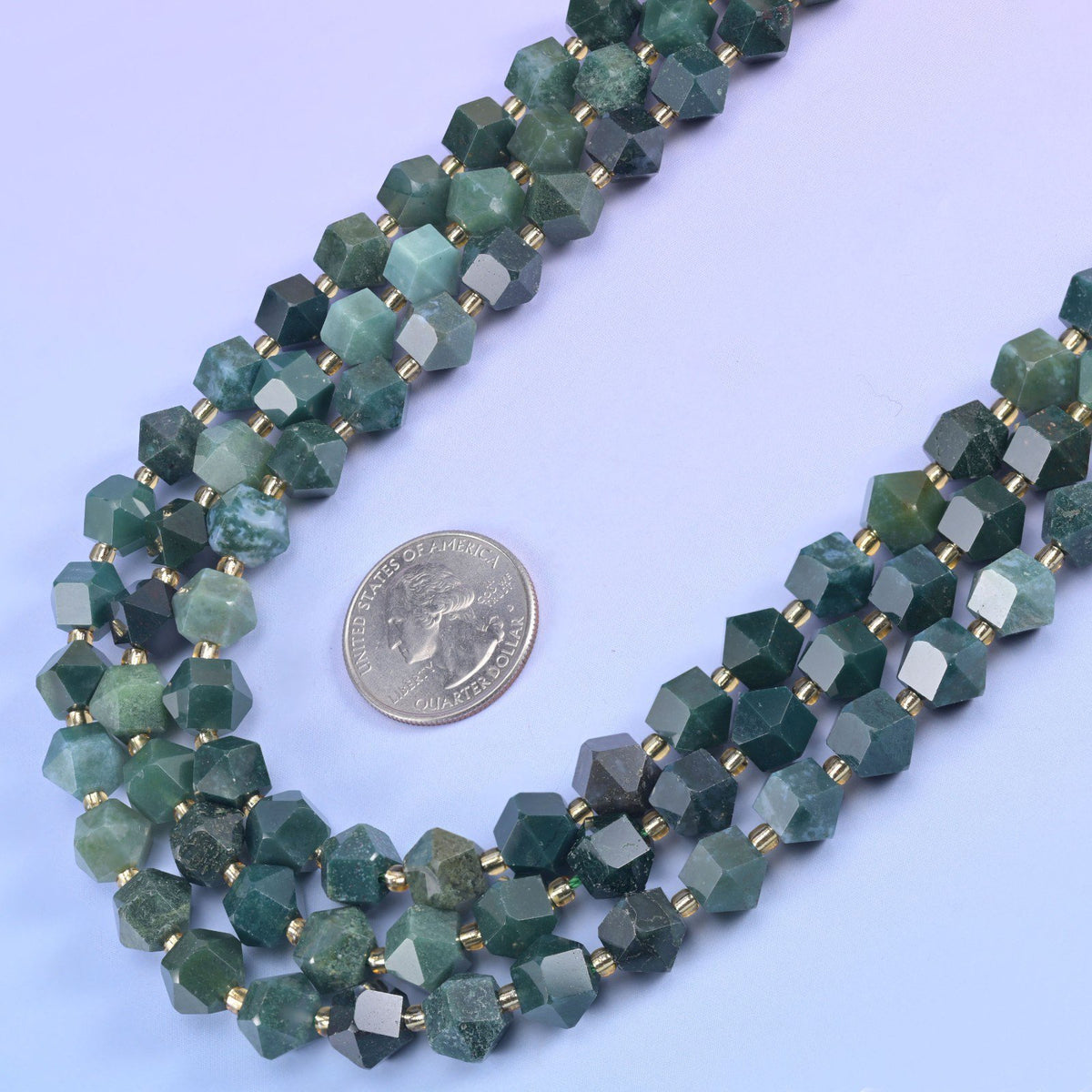 Faceted 8 sides diamond rhombus beads in moss agate beside a US quarter laid flat for scale.