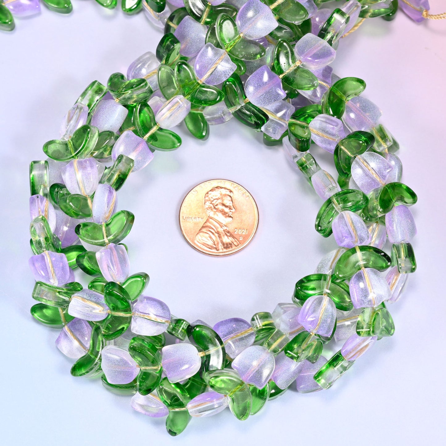 Bundled circular coil of tulip and leaf glass bead strands on a lavender background with a penny placed at the center for scale.