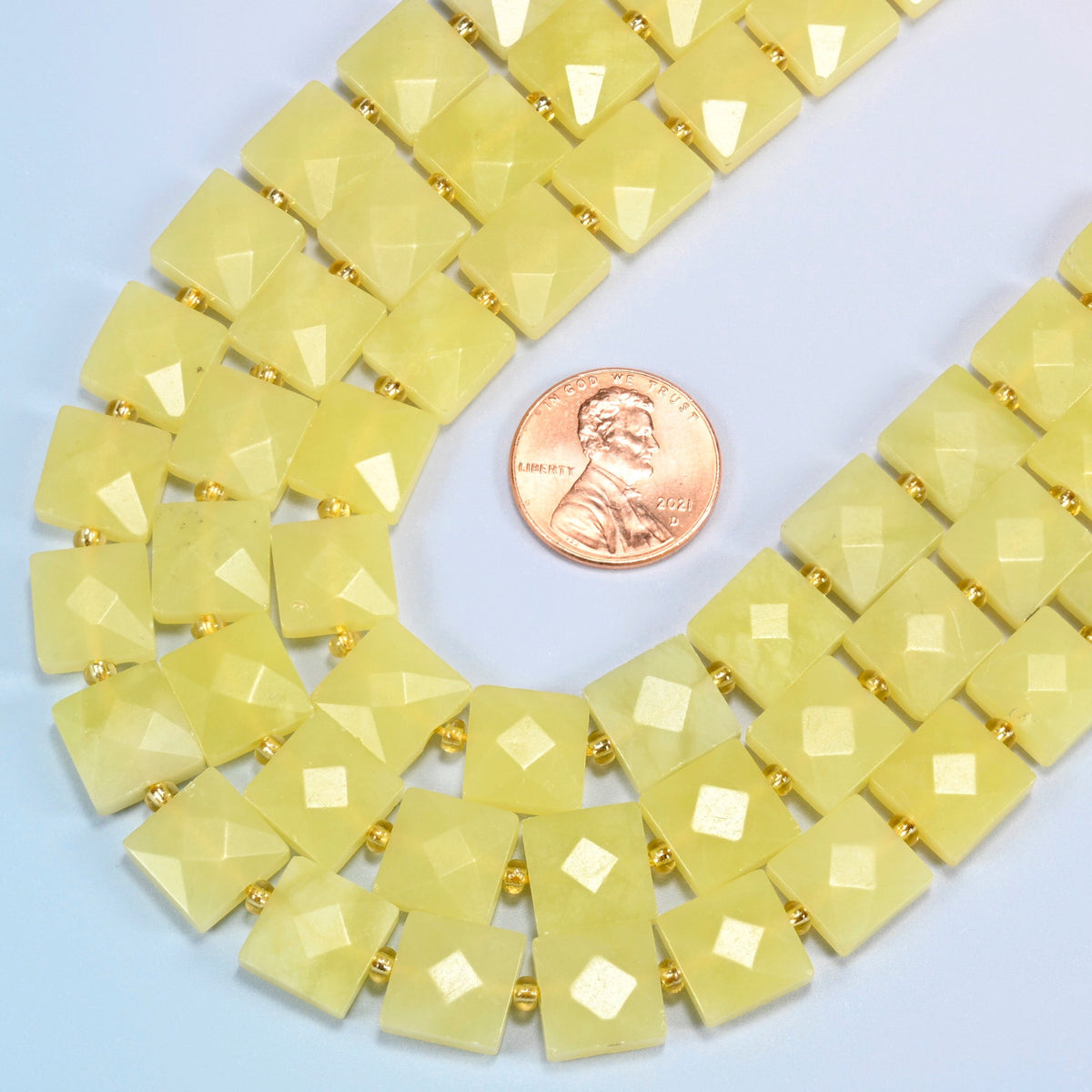 Close view of Lemon Jade faceted flat square strands curving beside a US penny for scale
