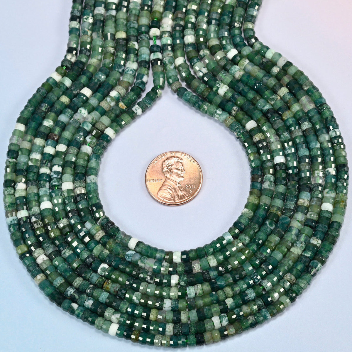 Moss agate faceted heishi disc strands formed into a teardrop loop around a US penny for scale