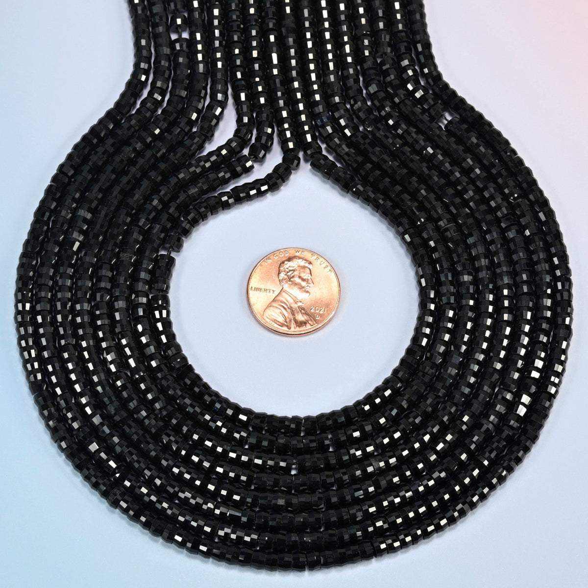 Black onyx faceted heishi disc strands formed into a teardrop loop around a US penny for scale