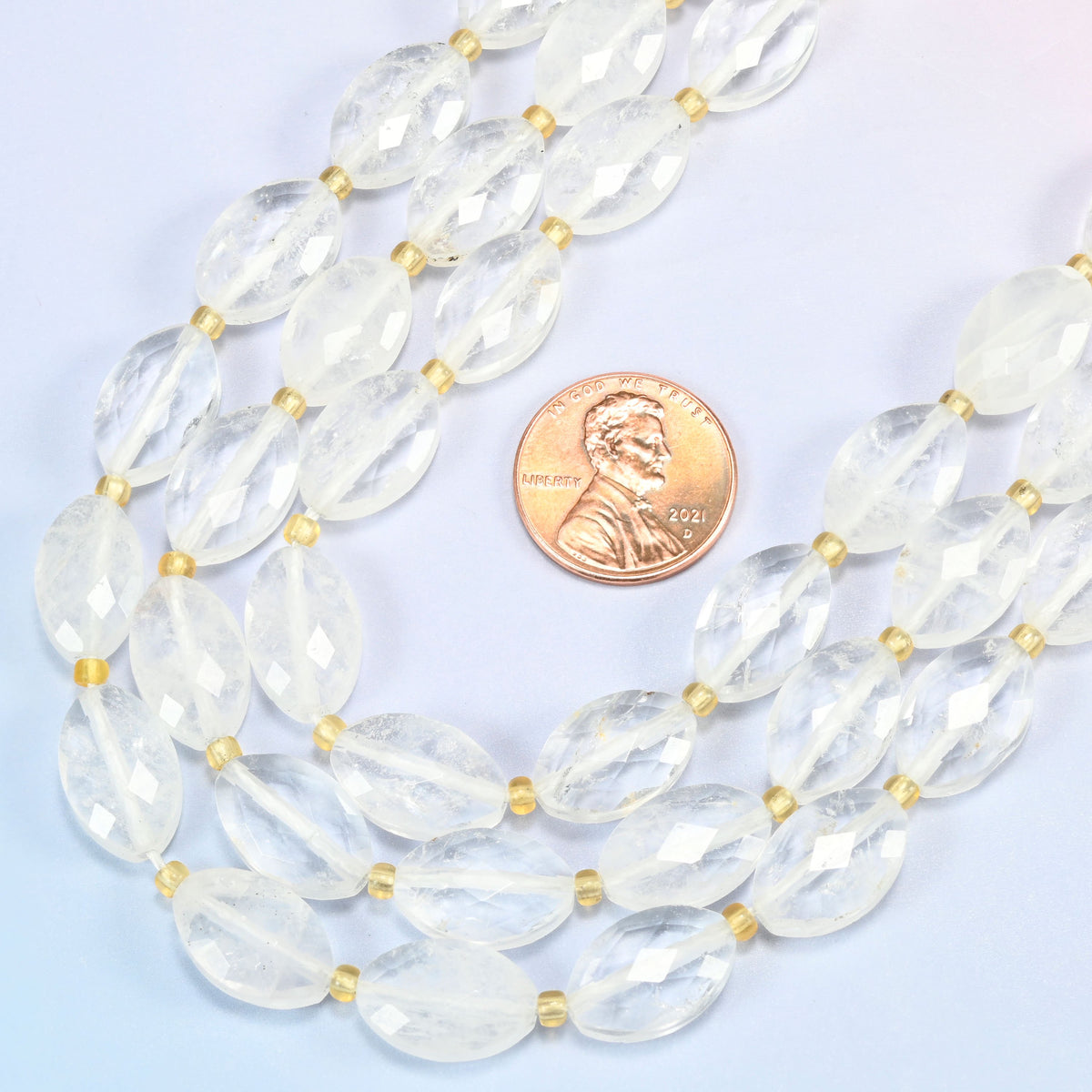 Close view of clear quartz faceted flat oval strands curving beside a US penny for scale