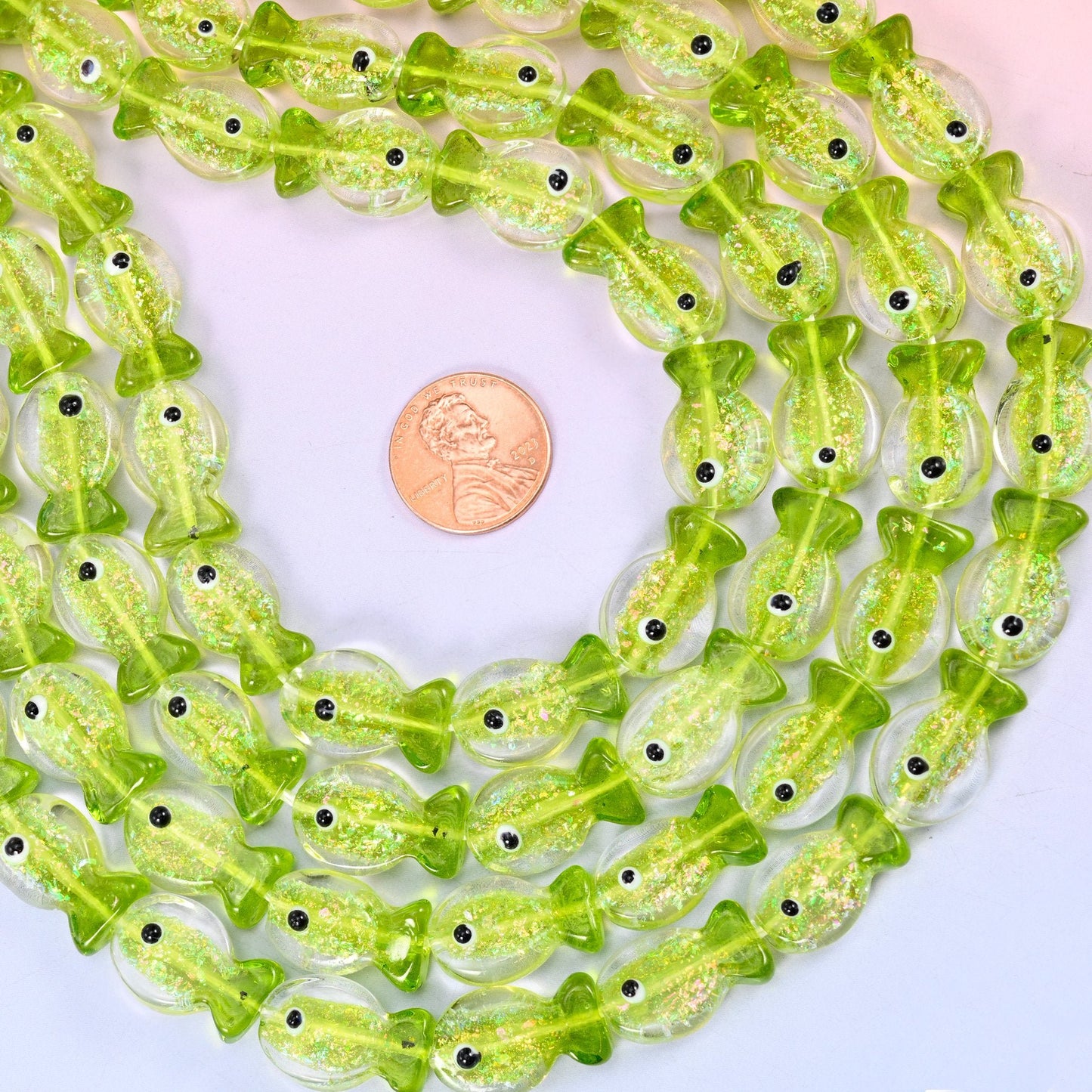 Iridescent Lime Green Fish Glass Beads — a small moulded fish in bright translucent lime, packed with fine glitter that catches the light from inside, with a clear tail and a single black eye dot.