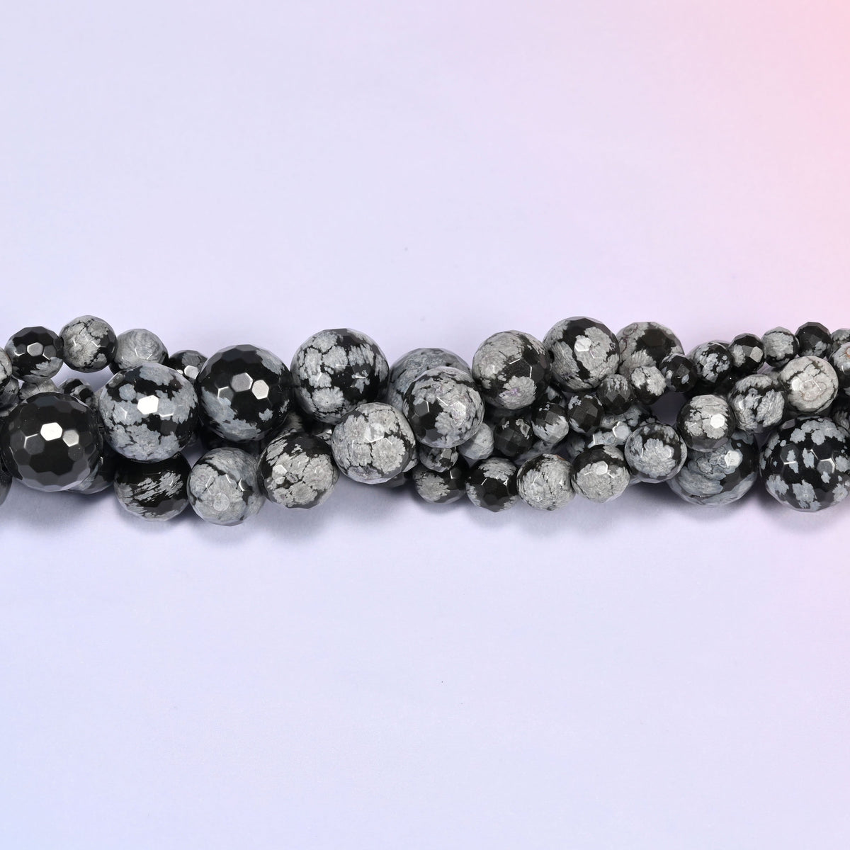 Close-up of a single row of Snowflake Jasper faceted round beads, showing the faceted cut and the stone's mottled black and gray coloring.