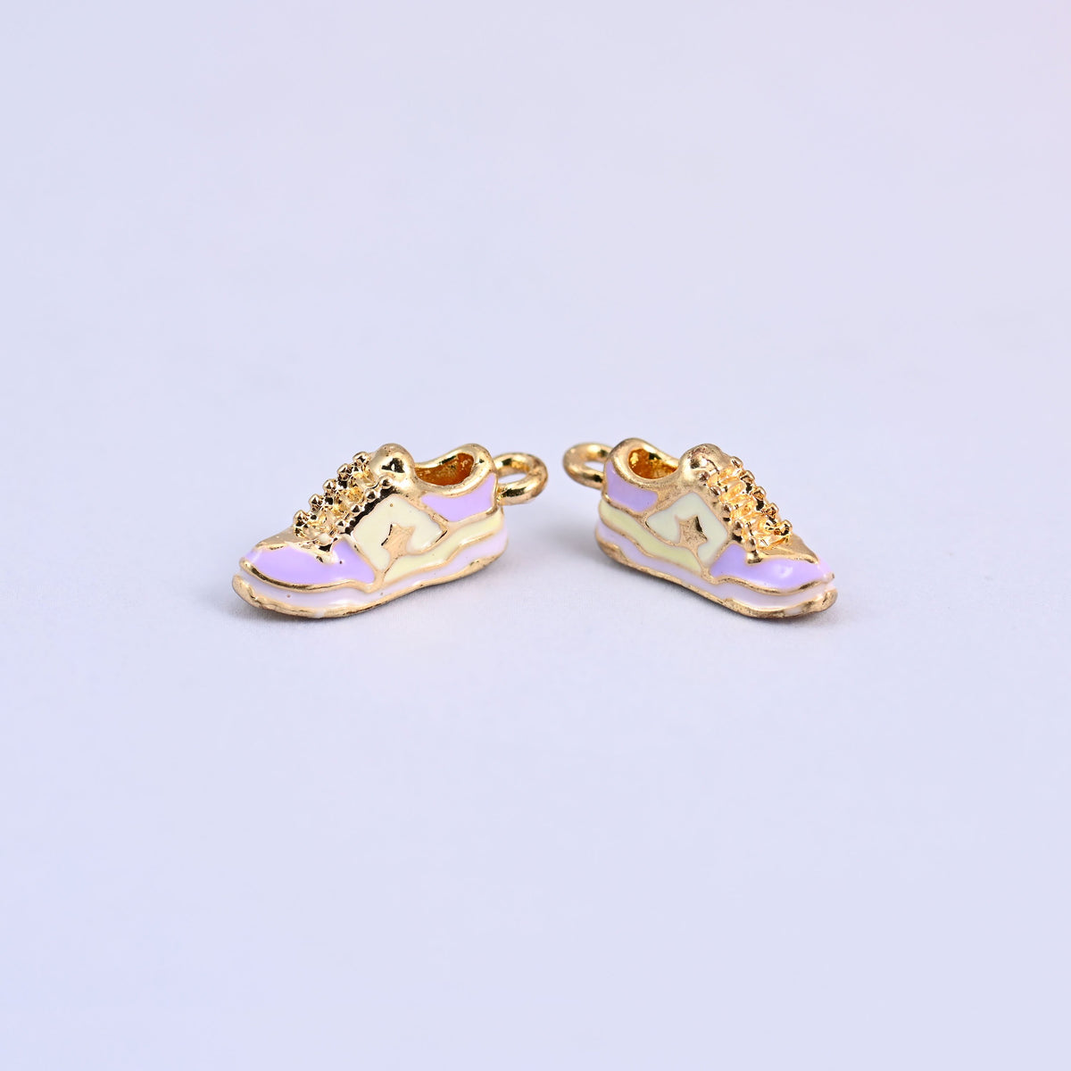 Two light purple sneaker charms with light yellow panels and gold laces.