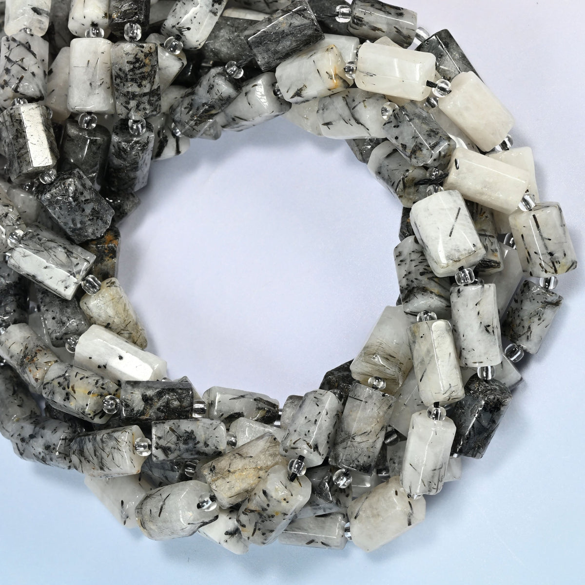 Black rutilated quartz faceted tube beads coiled into overlapping loops, whole strands of white and black stone