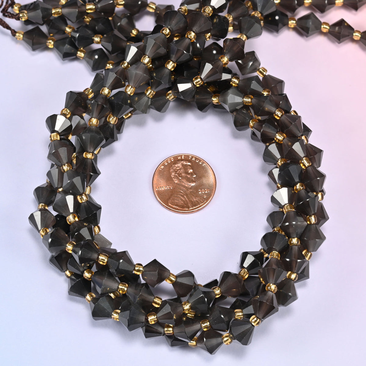 Ice Obsidian faceted bicone beads 8mm with gold-tone spacers, strand coiled with a penny centered, close-up of the beads