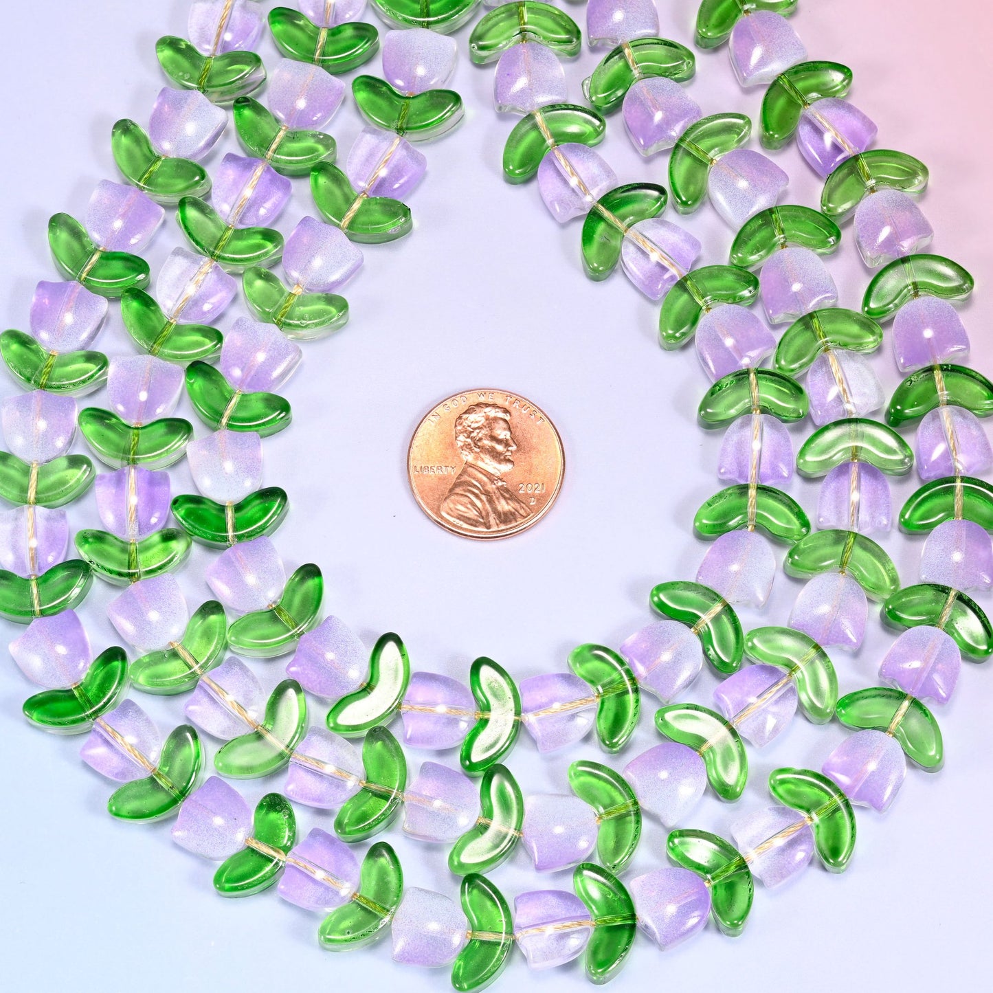Close-up of a circular coil of lavender tulip and green leaf glass beads, showing the dense flower and leaf pattern.