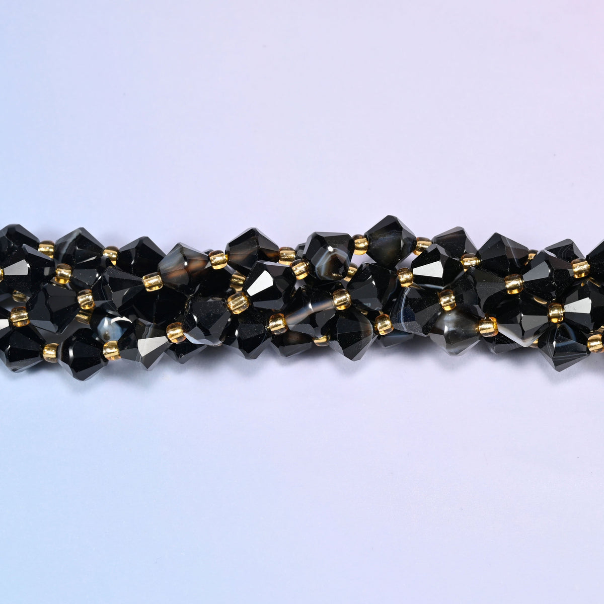 Dyed black strip agate bicone beads shown as a single strand laid straight across, the applied black staying even while the stripe pattern differs bead to bead.