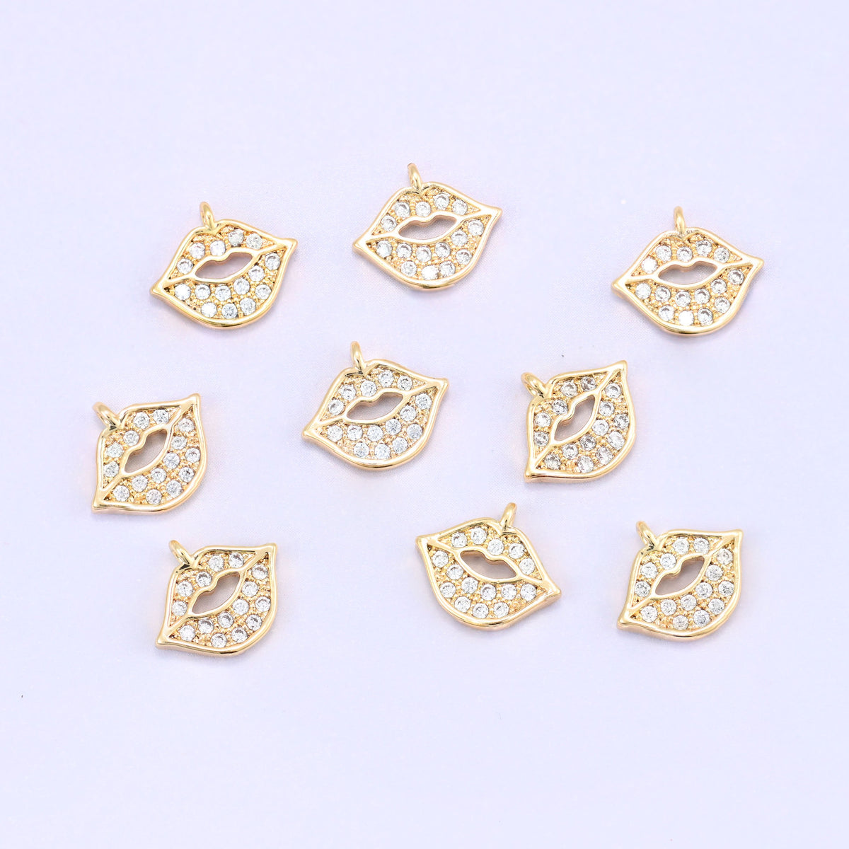 Small gold charms, nine gold plated lip charms with clear cubic zirconia scattered on a pale backdrop