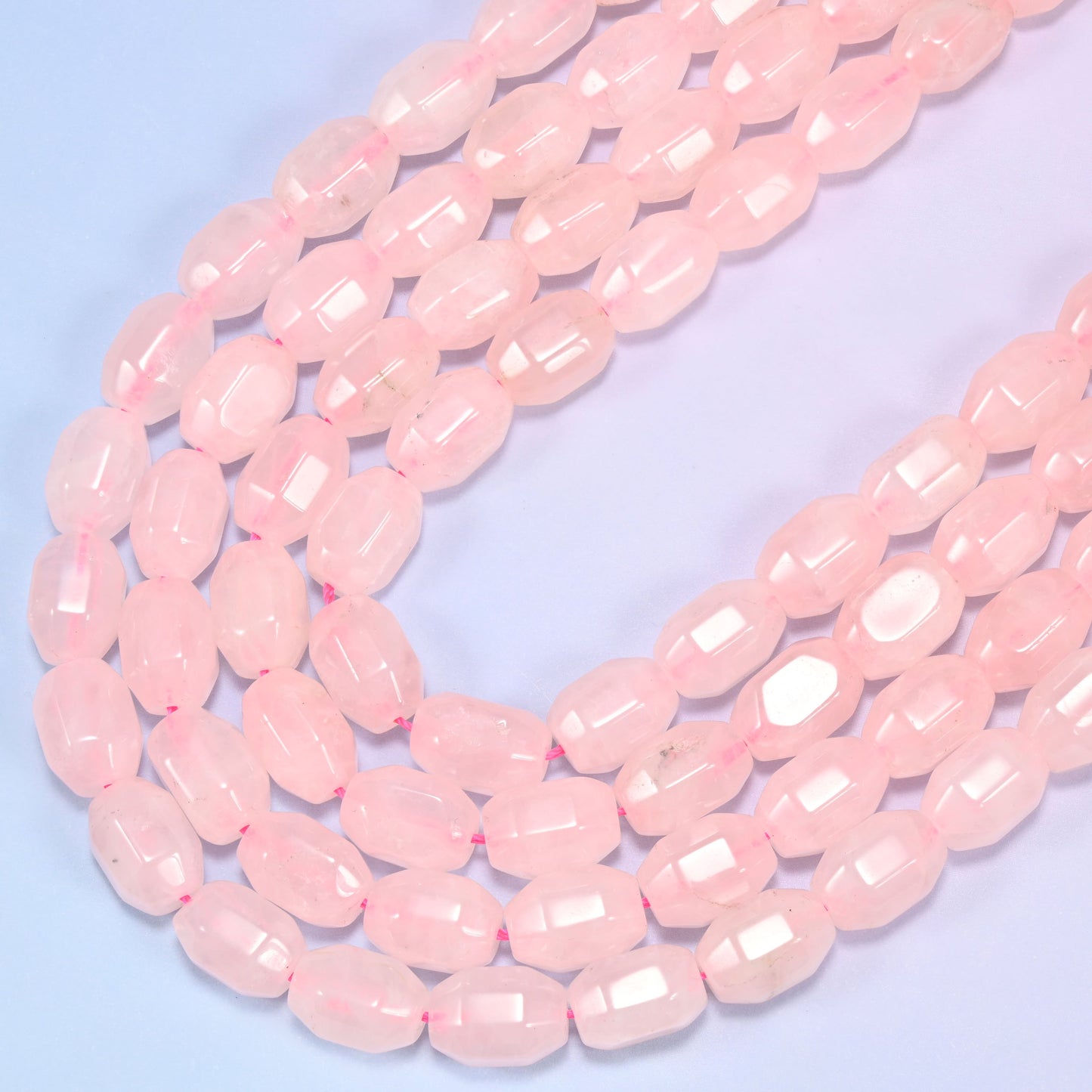 Close-up of a circular coil of Rose Quartz faceted barrel beads on a light blue background.