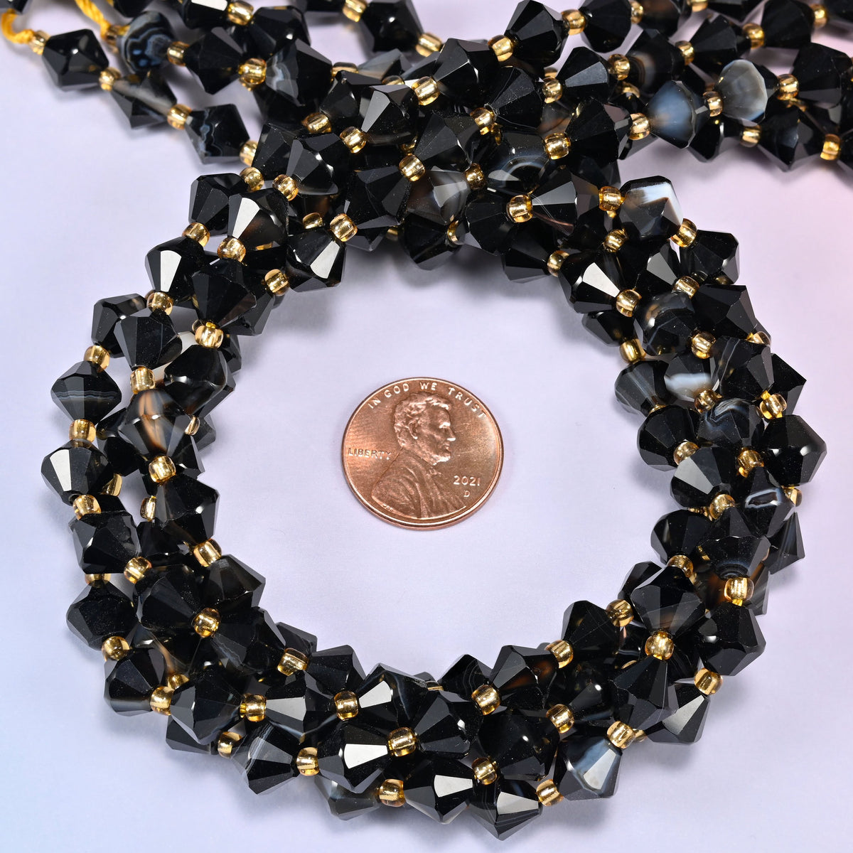 Dyed black strip agate bicone beads coiled into a round ring, 8mm beads with gold-tone spacers throughout.