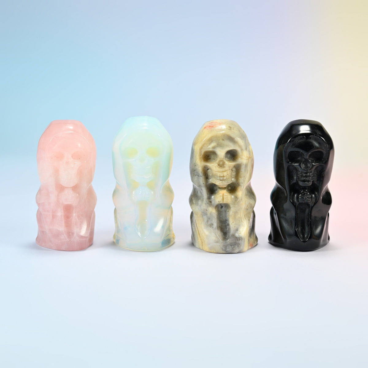Four hooded skull carvings in a row: natural rose quartz, opalite, natural crazy agate and natural black obsidian