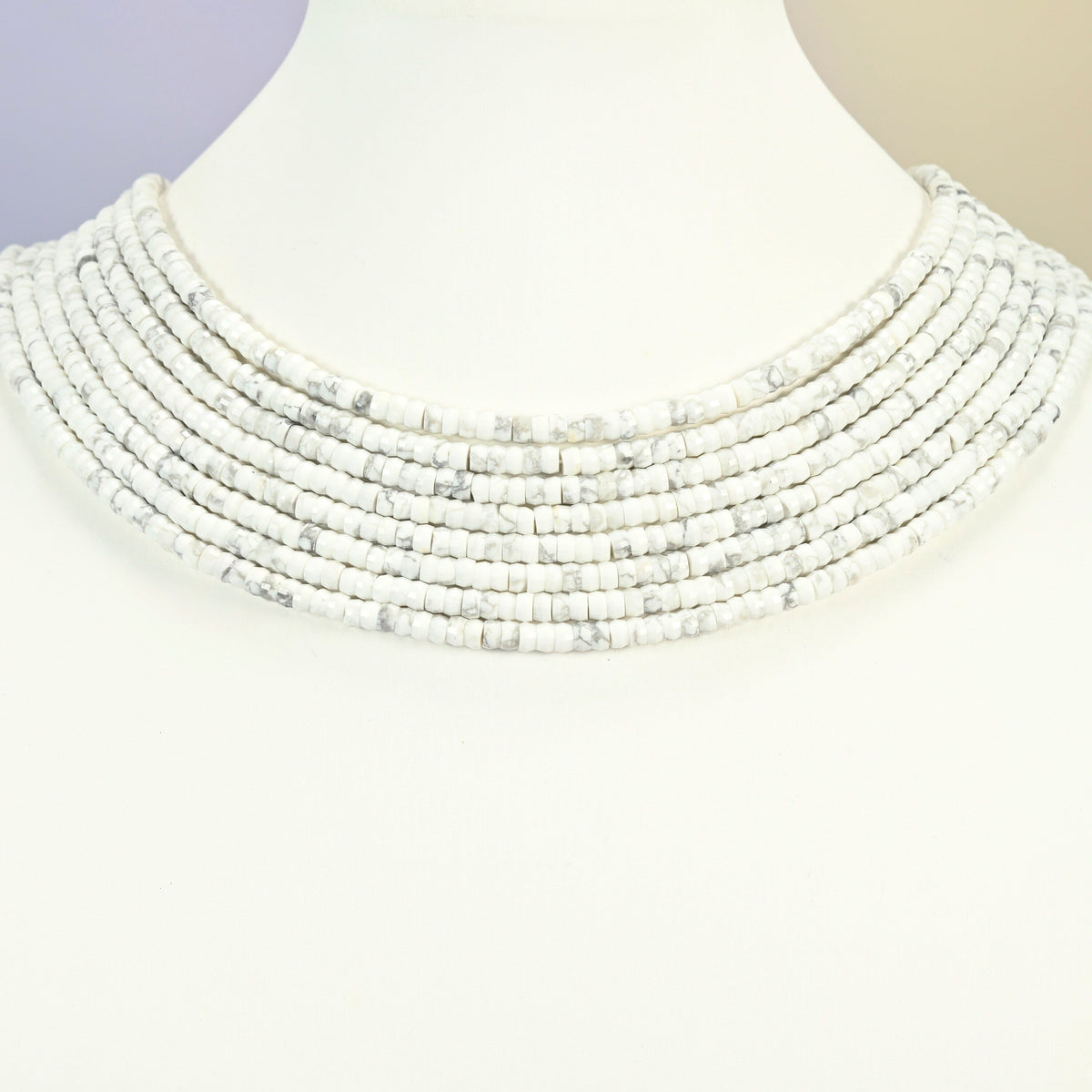 White howlite faceted heishi disc strands arranged as a layered collar on a white display bust, white beads across the neck