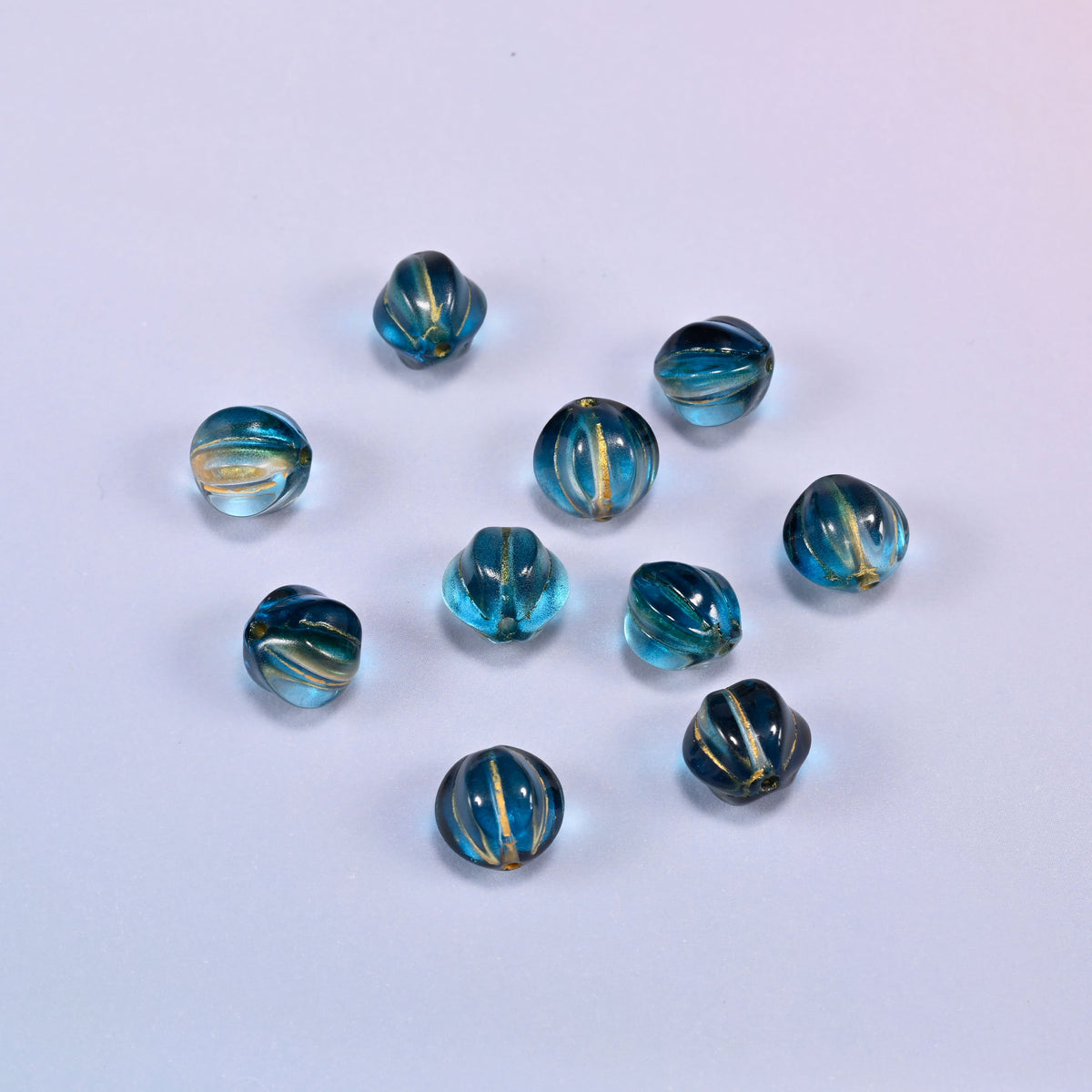 A scattered group of loose 8mm dark blue gold pumpkin glass beads, showing the melon ribs and the drill holes.