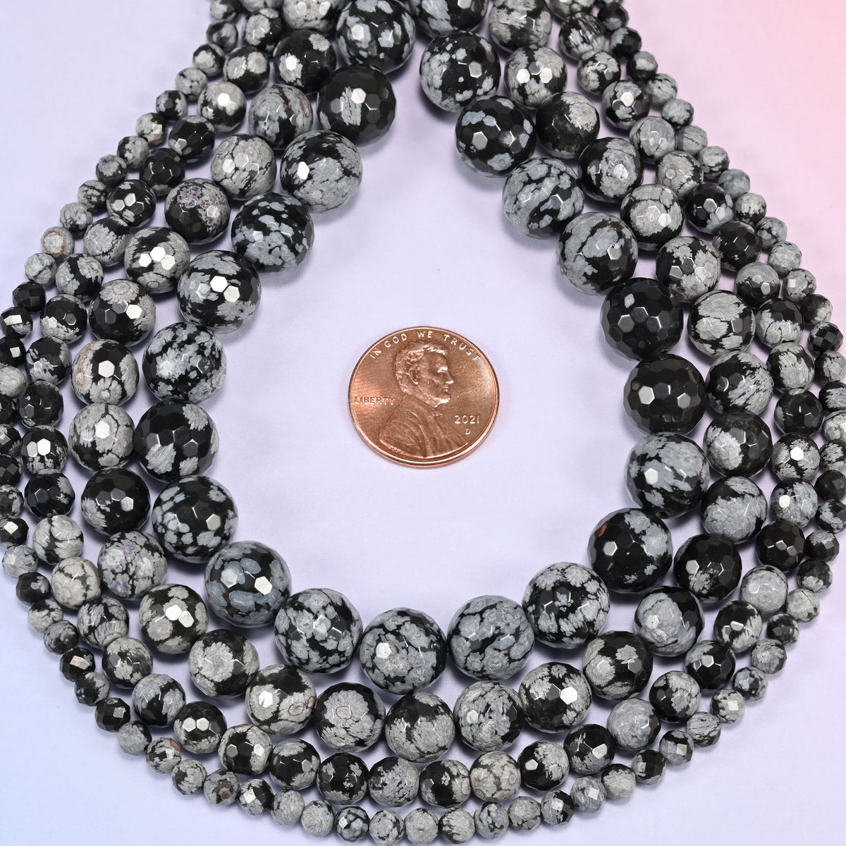 Snowflake Jasper faceted round beads coiled into a loop with a penny resting near the center for scale.