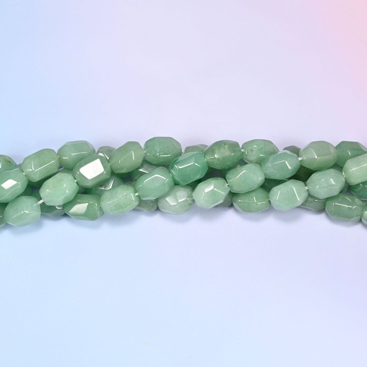 Close-up circular coil of green faceted Aventurine barrel bead strands on a lavender background with a penny in the center for size comparison.