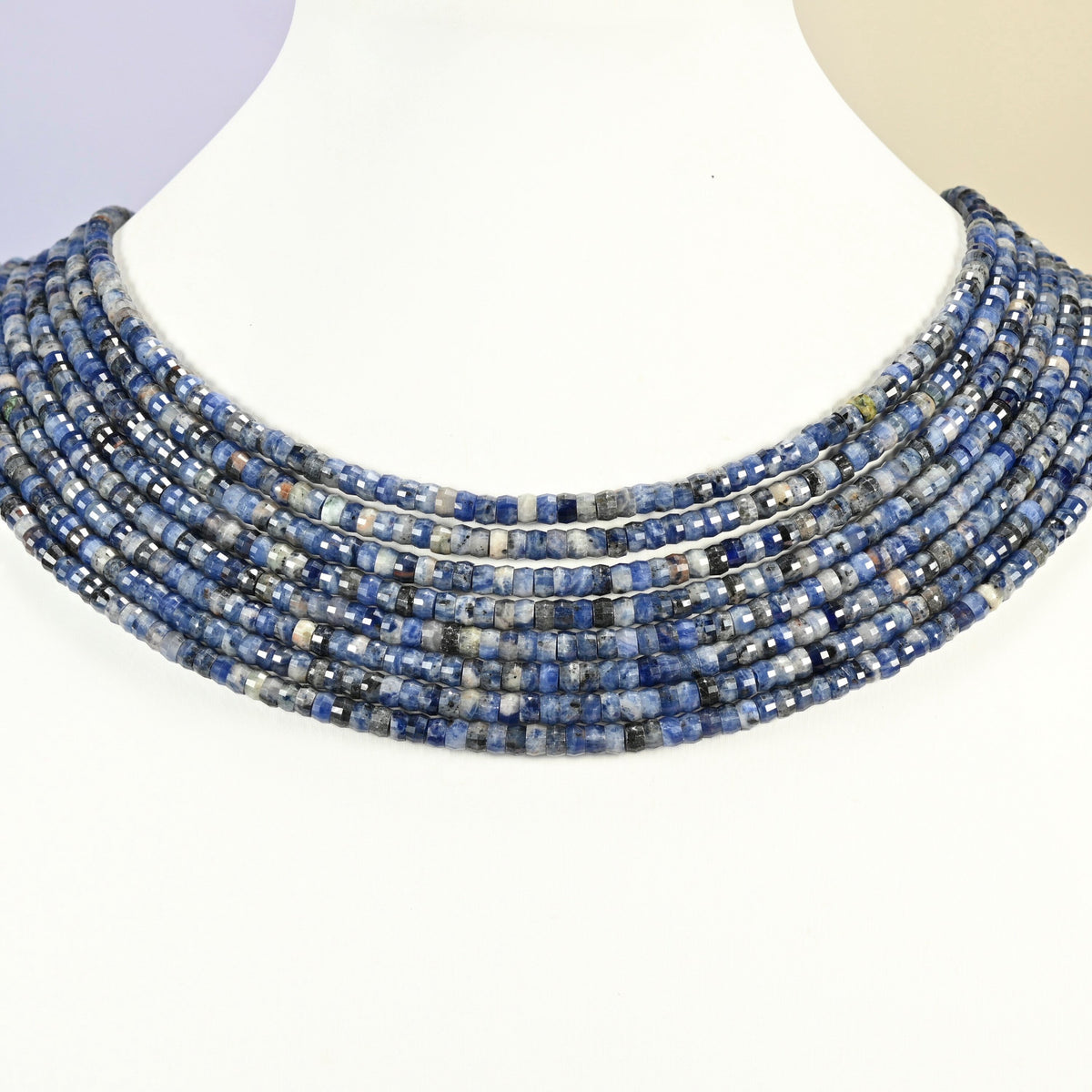 Sodalite faceted heishi disc strands arranged as a layered collar on a white display bust, blue and white beads across the neck