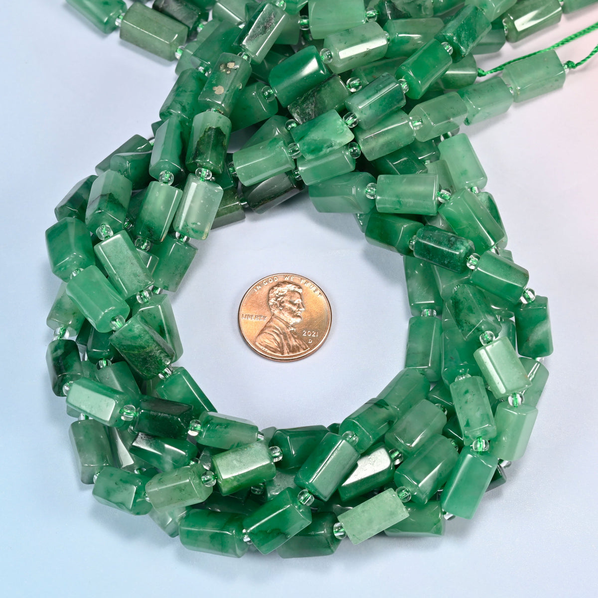 African jade faceted tube beads 7x11-7x12mm coiled in a loop around a US penny for scale, close-up of the faceted tube shape