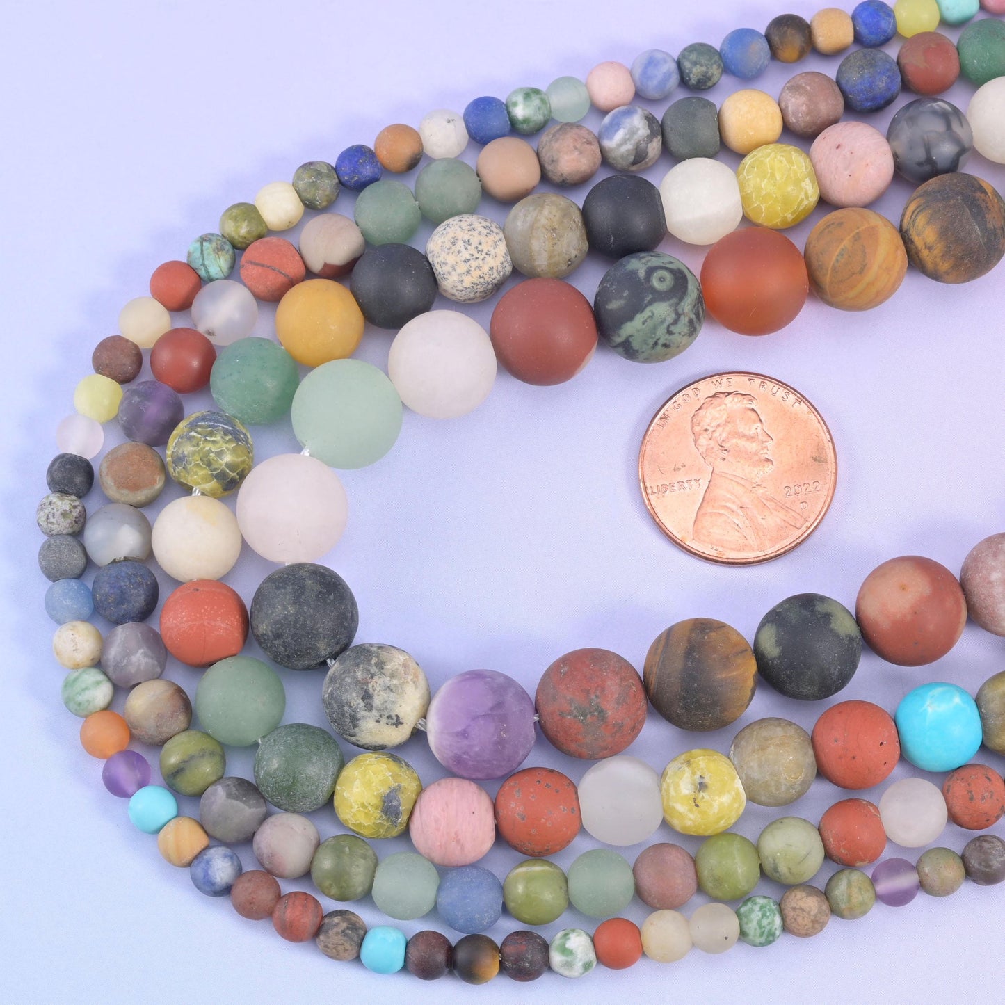 Assorted matte round beads looped around a US penny for size comparison